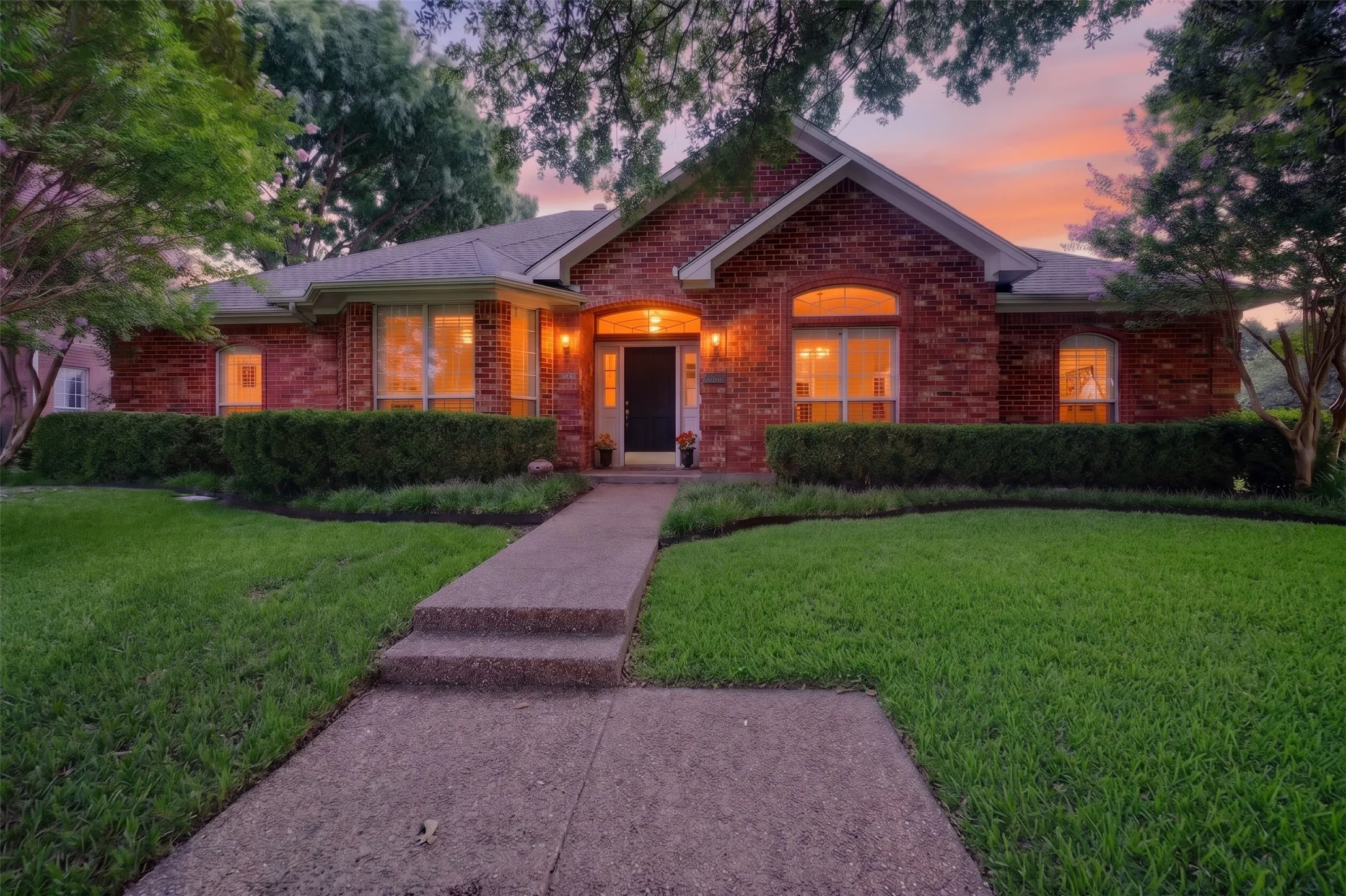 Brick exterior with arched entryways, a bay window, mature trees, and a concrete walkway
