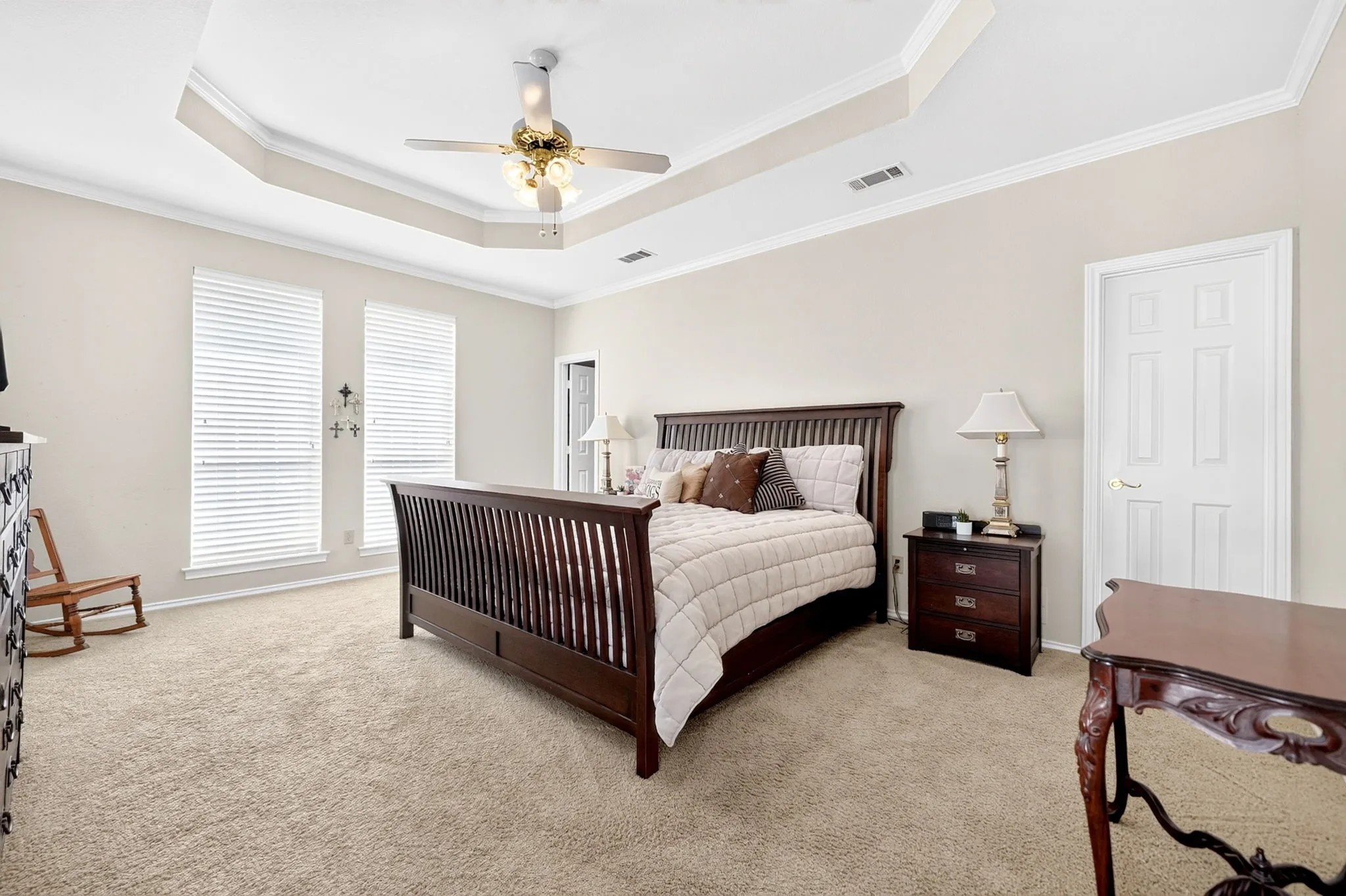 Tray ceiling with a ceiling fan, two windows with blinds, light-colored carpet, and a paneled door