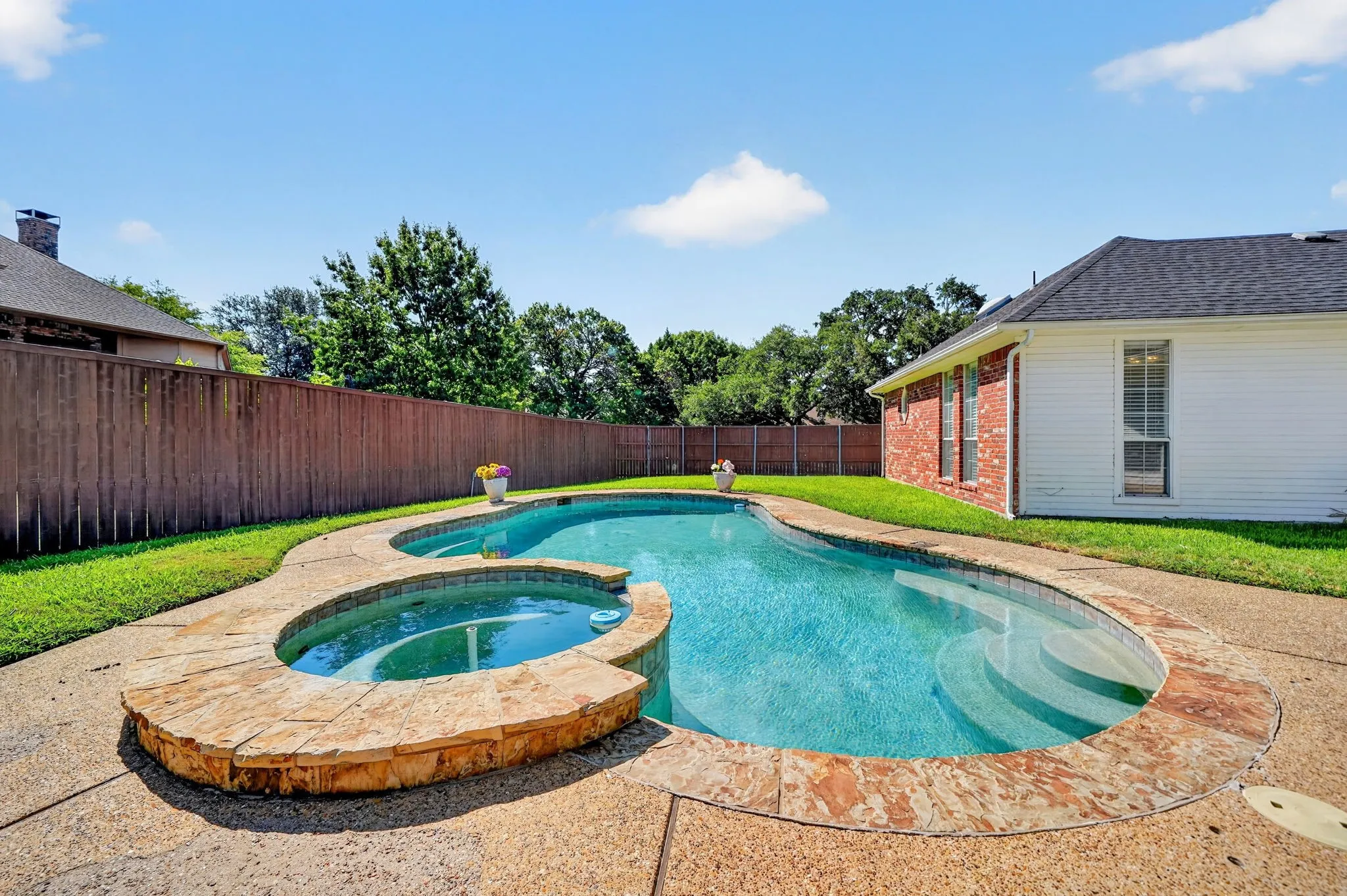 Backyard oasis featuring a freeform swimming pool with integrated spa, stone coping, and concrete decking, all surrounded by a private wood fence