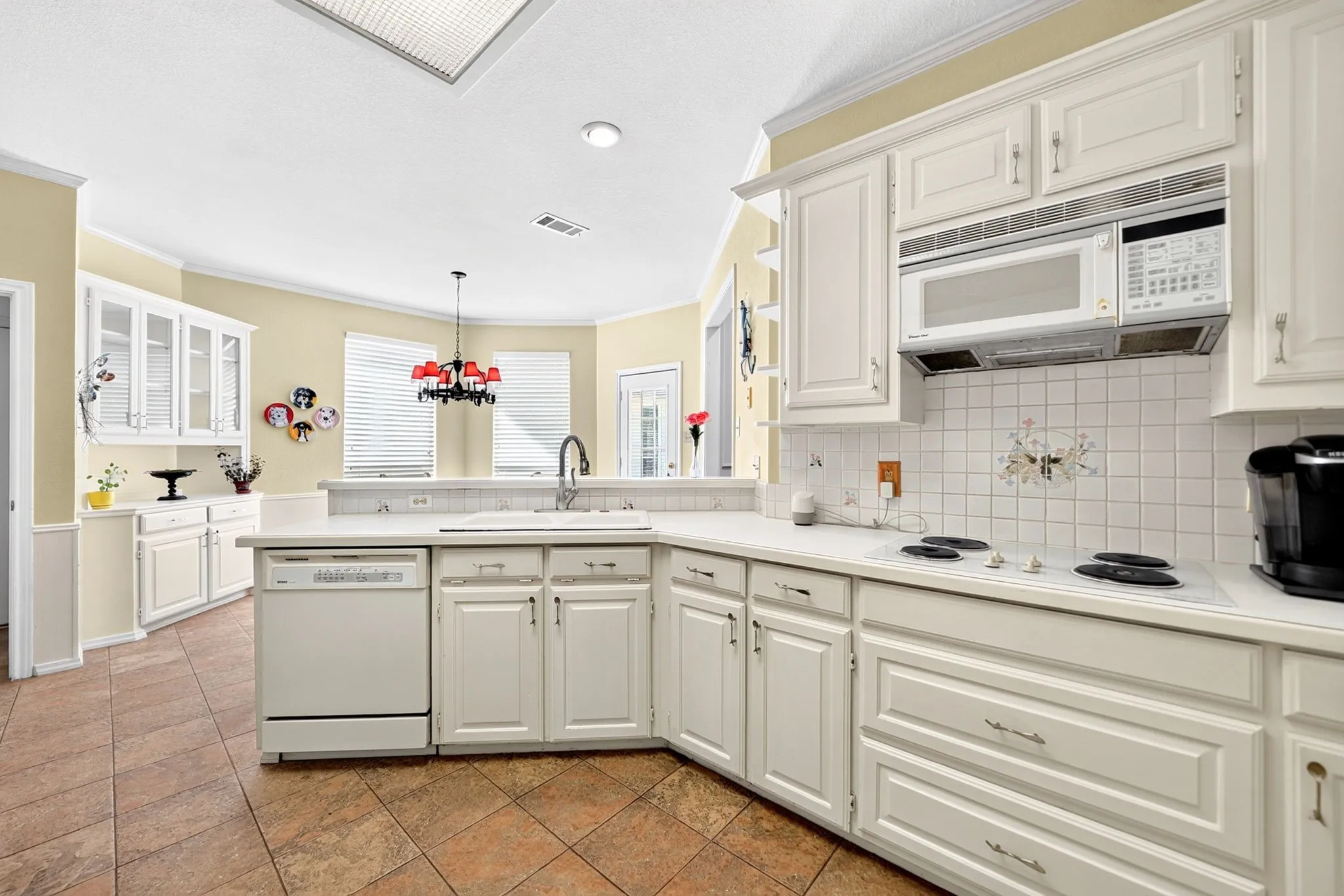 Kitchen featuring white cabinetry, a built-in dishwasher, an over-the-range microwave, a tile backsplash, and tile flooring