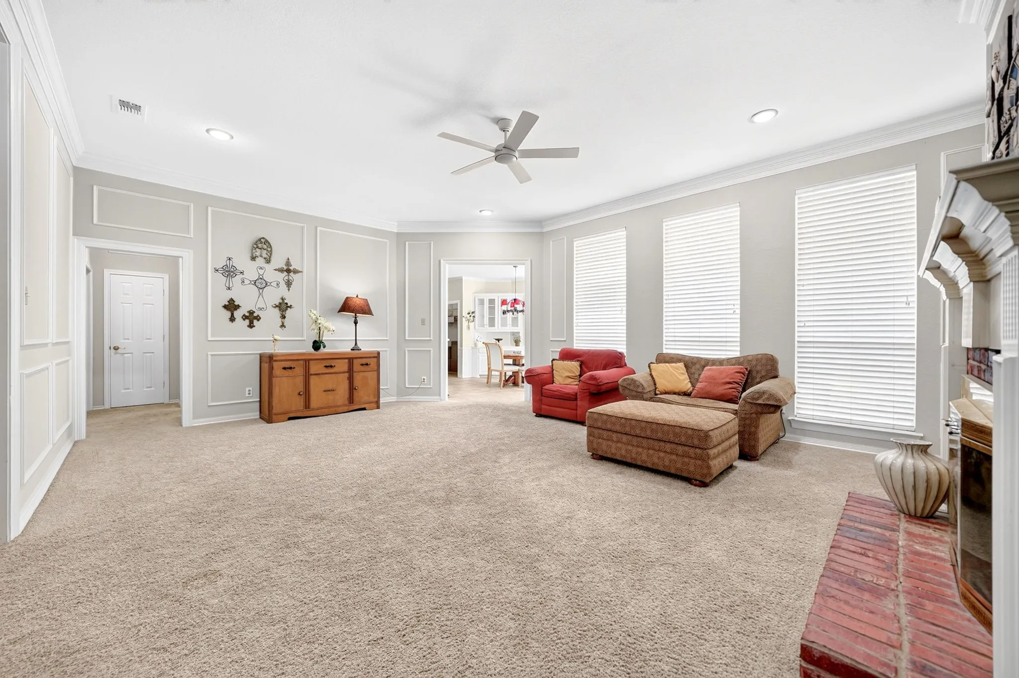 Spacious living area featuring neutral carpeting, decorative wall molding, recessed lighting, a ceiling fan, and multiple windows with blinds