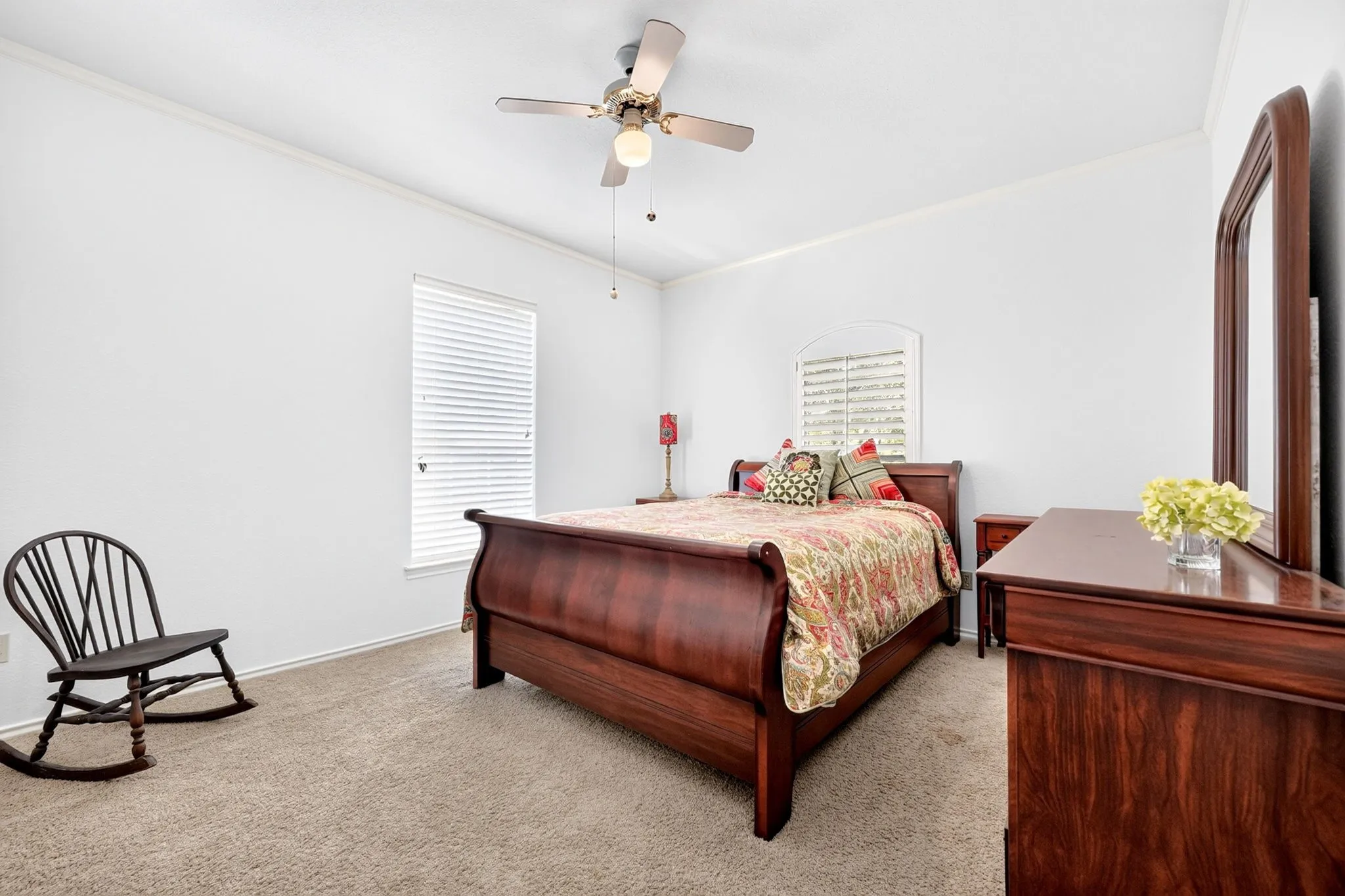 Carpeted flooring, white walls, ceiling fan with light fixture, window with blinds, and an arched window with louvered shutters