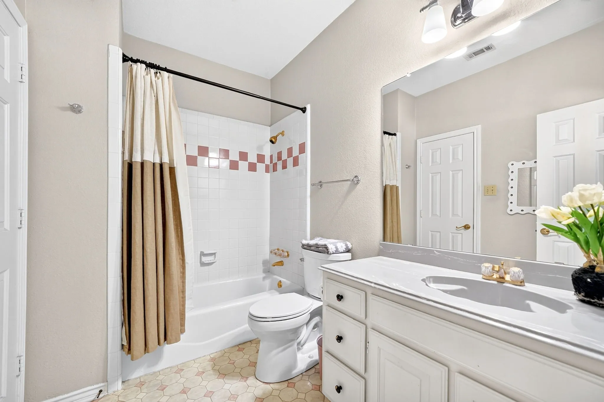 Bathroom featuring a single vanity with built-in cabinetry, an integrated sink, a large wall-mounted mirror, and a bathtub with a tiled shower surround