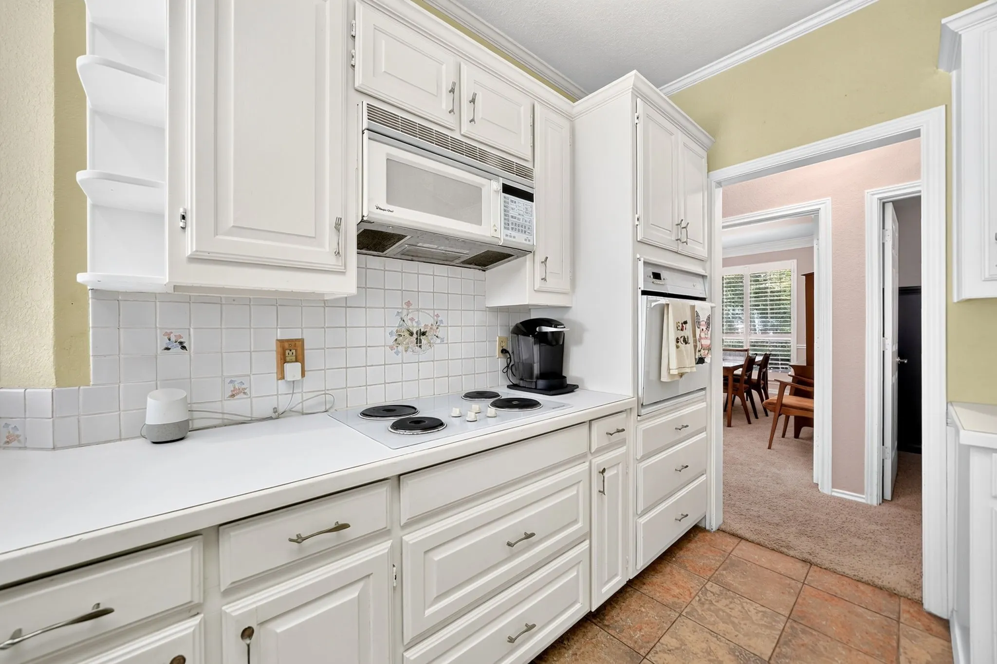 White cabinetry with panel detailing, integrated wall oven, built-in microwave, white tile backsplash, and tile flooring