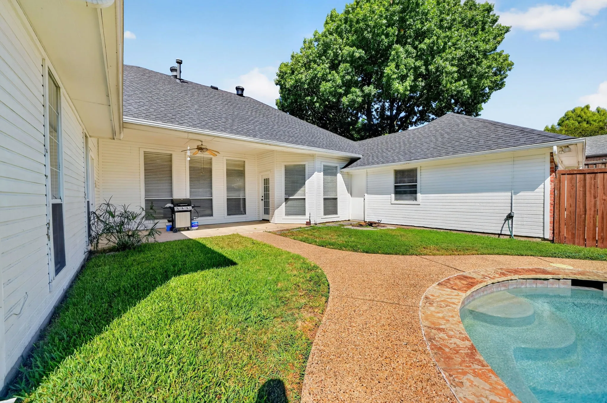 Backyard features an in-ground swimming pool, exposed aggregate pathway, a covered patio, and wood fencing