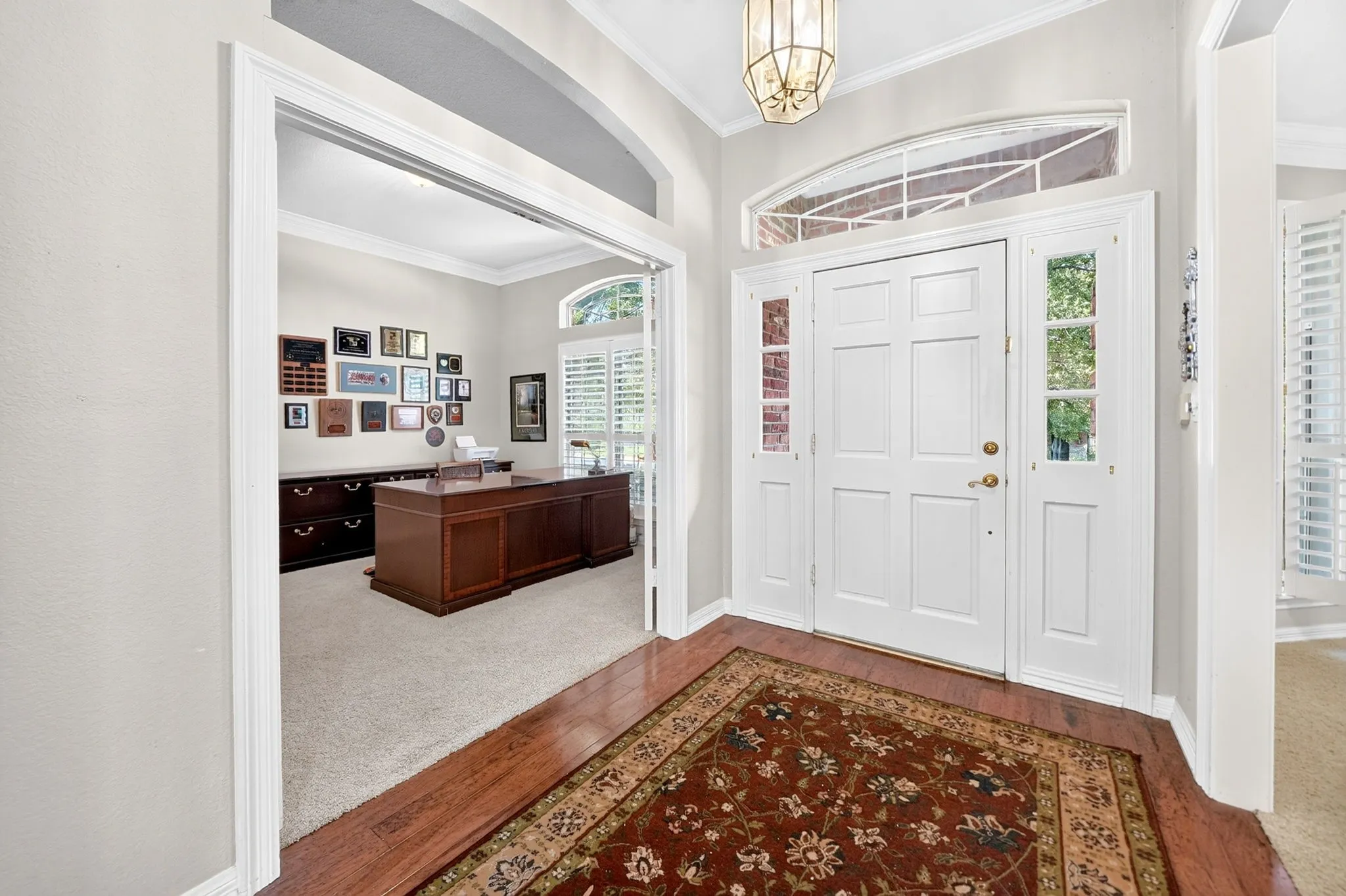 Entryway featuring a double-paneled door with sidelights, an arched transom window, wood-finish flooring, and crown molding