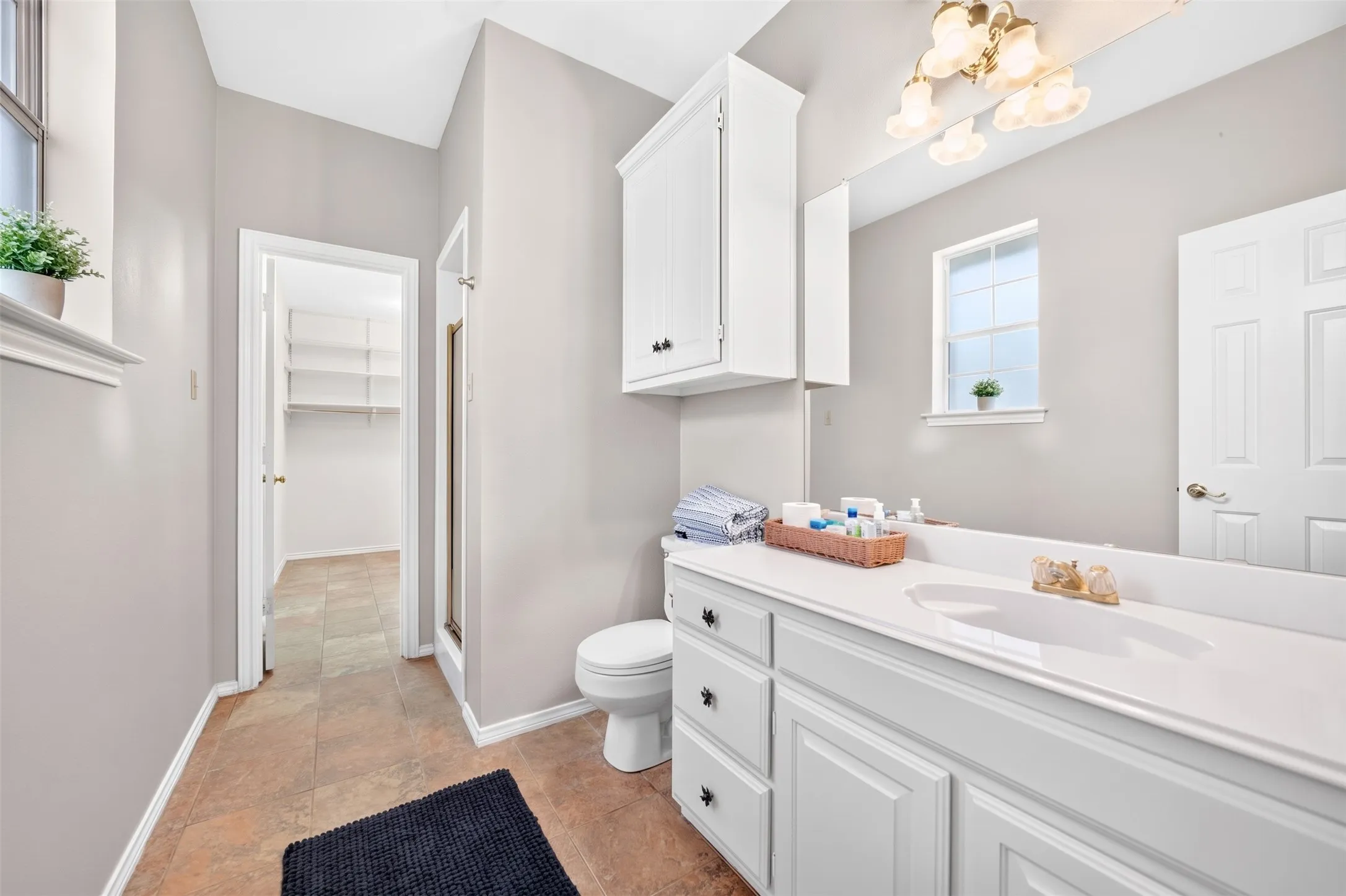 Light-toned tile flooring, built-in vanity with white cabinetry, white solid surface countertop with integrated sink, white built-in upper cabinet, and a walk-in closet with built-in shelving