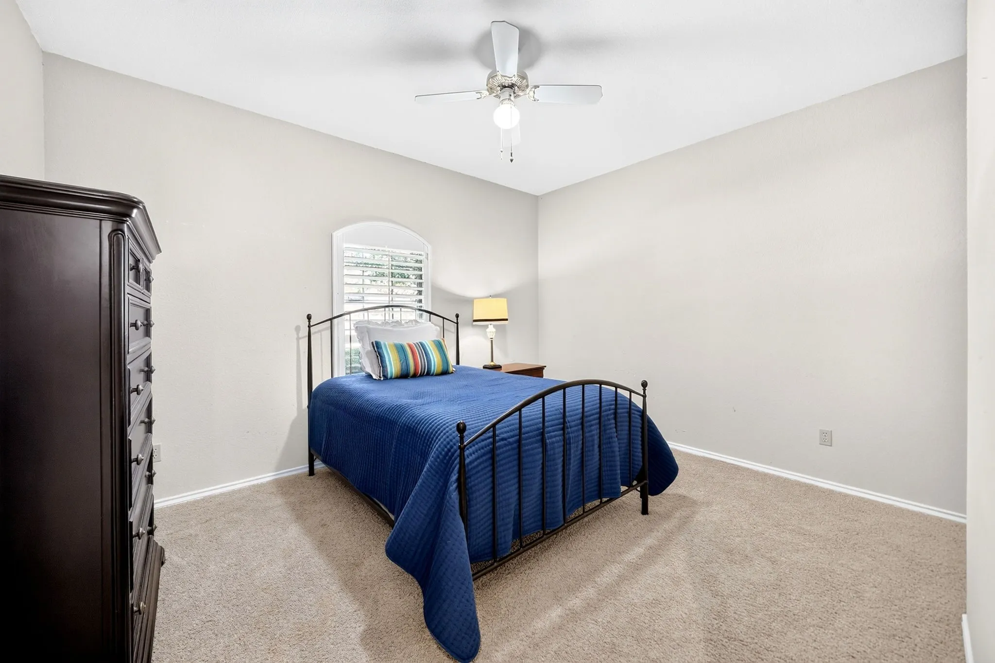 Carpeted room with a vaulted ceiling, ceiling fan, and an arched window featuring plantation shutters