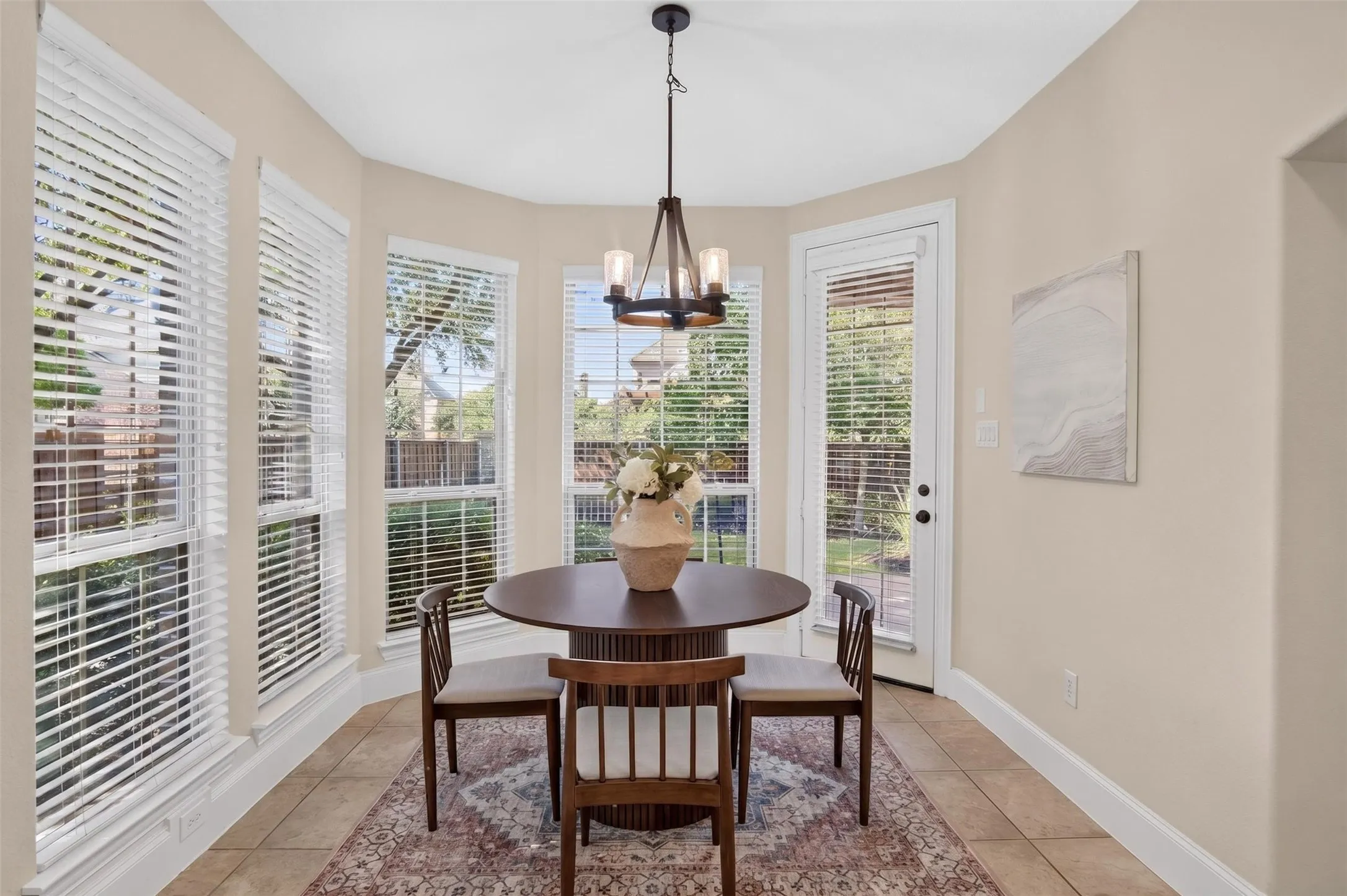 Sunlit dining room featuring expansive multi-pane windows with plantation shutters, hardwood-finish flooring, neutral wall finishes, and a pendant light fixture suspended from a coffered ceiling detail