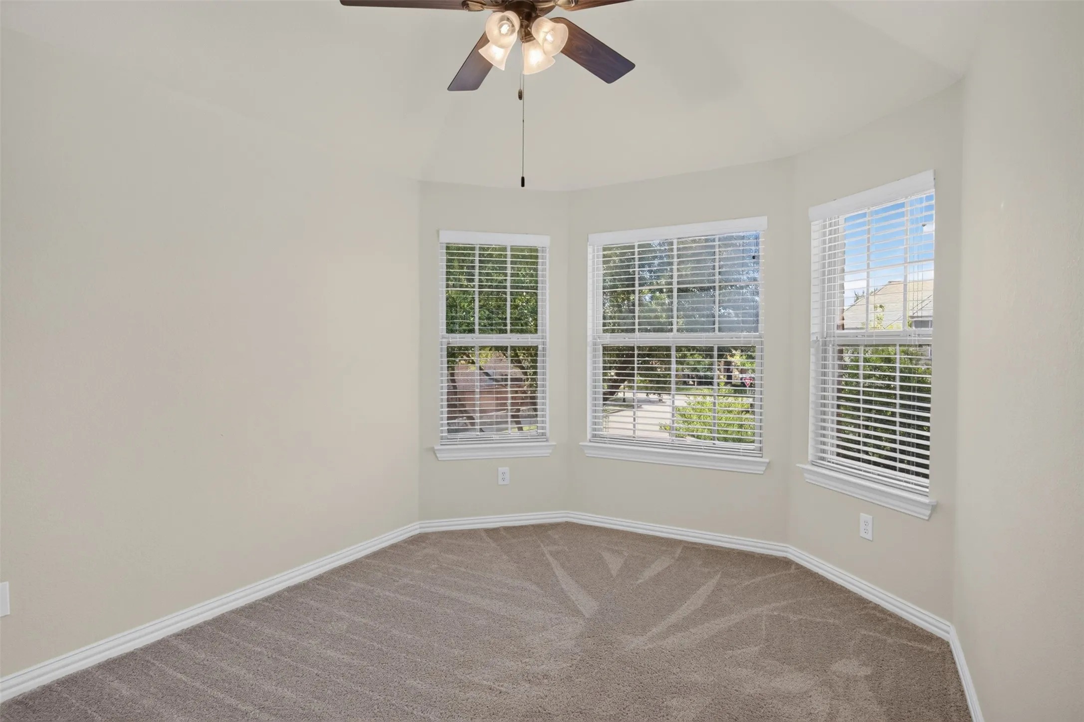 Angled wall featuring three windows with blinds, ceiling fan, and neutral-toned carpeting