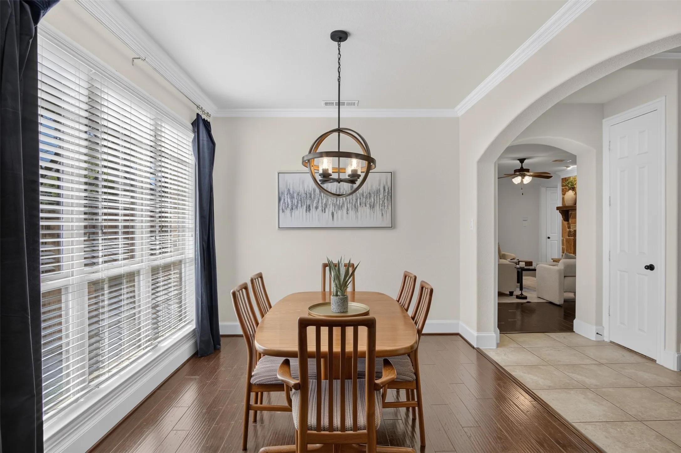 Wood-finish flooring, large multi-pane window, decorative ceiling light fixture, crown molding, and an arched doorway