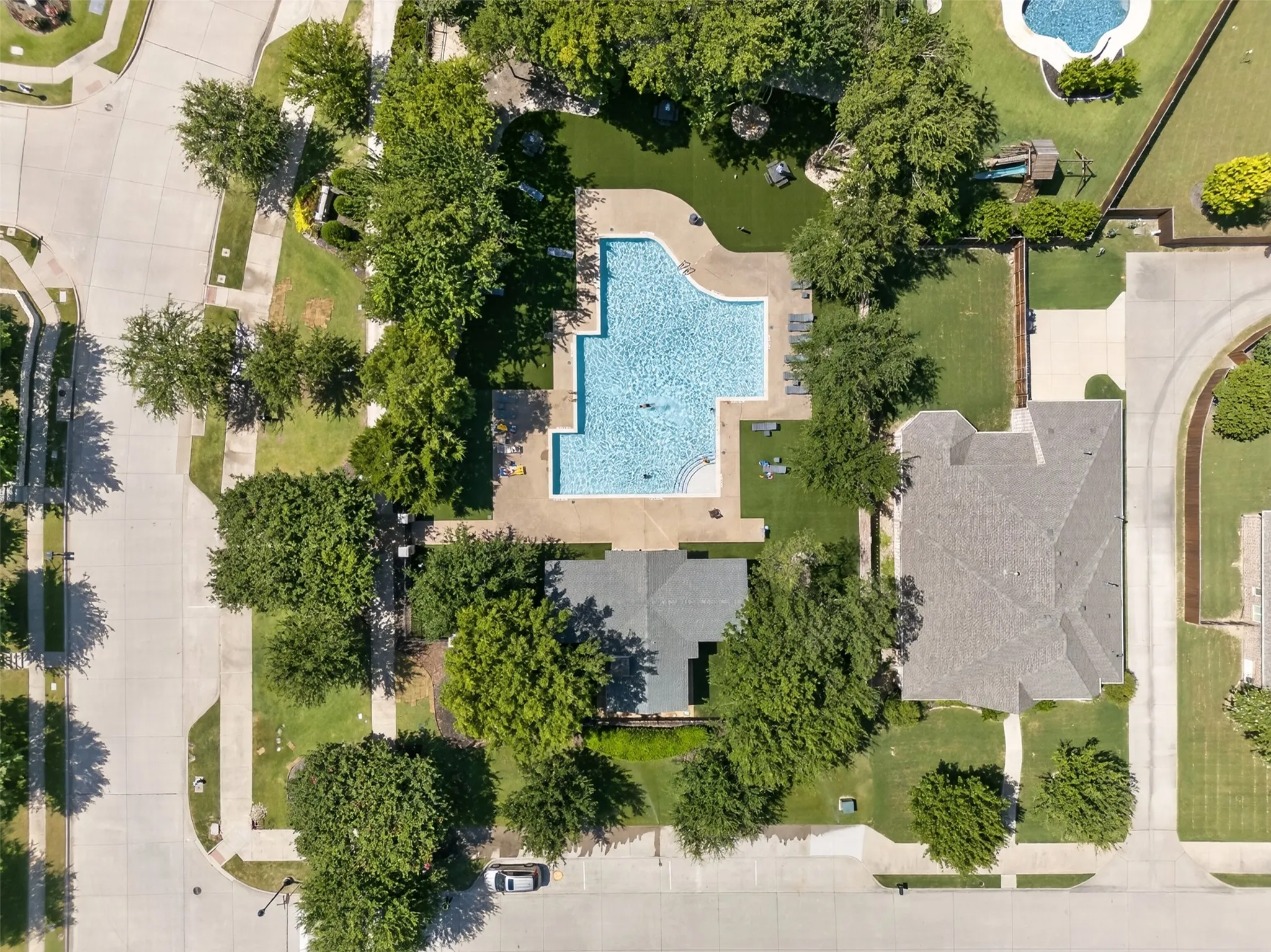Expansive outdoor space featuring a large swimming pool, surrounding paved patio, and mature trees