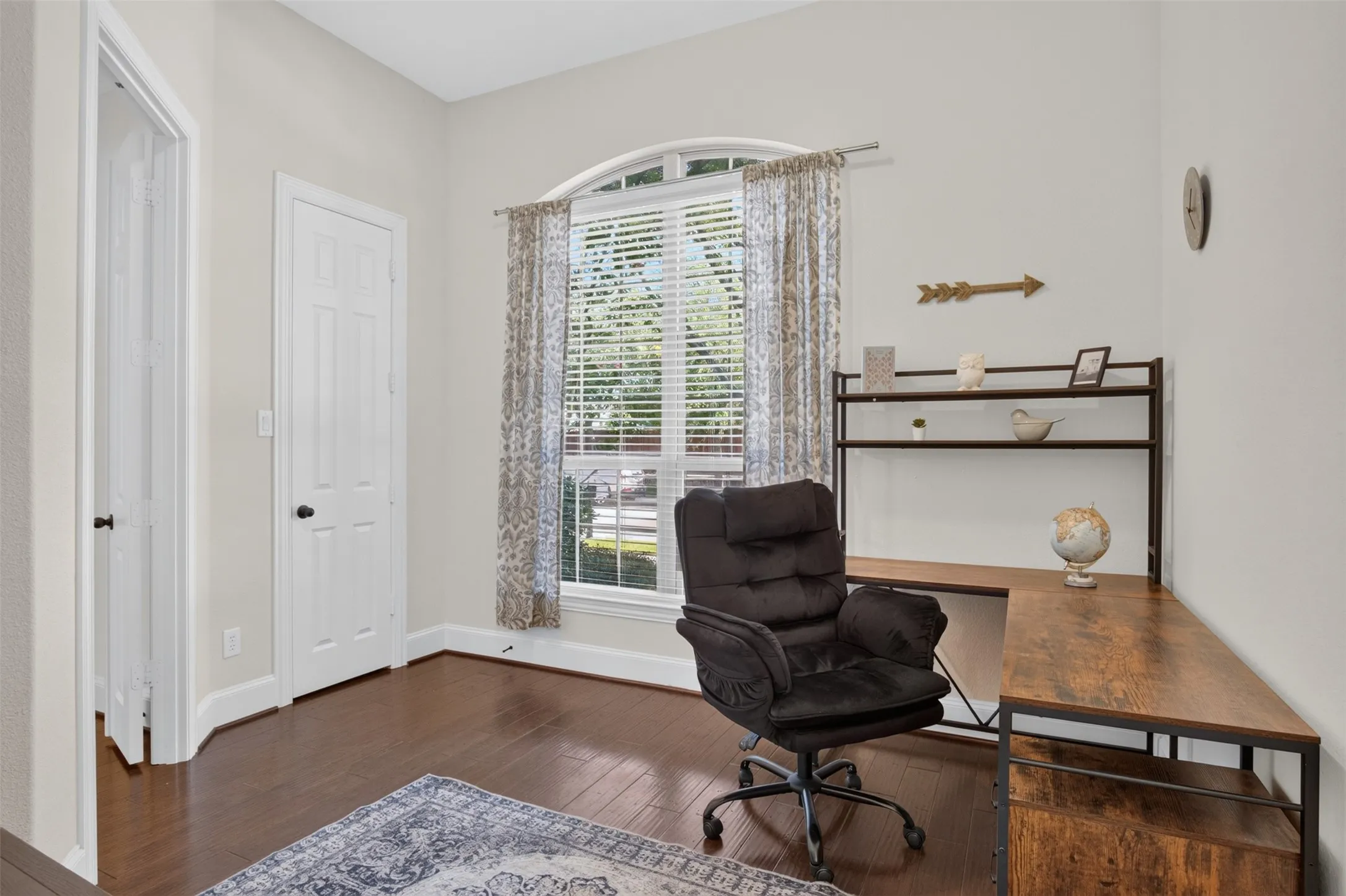 Arched window with blinds, wood-finish flooring, white paneled doors, and light neutral wall paint