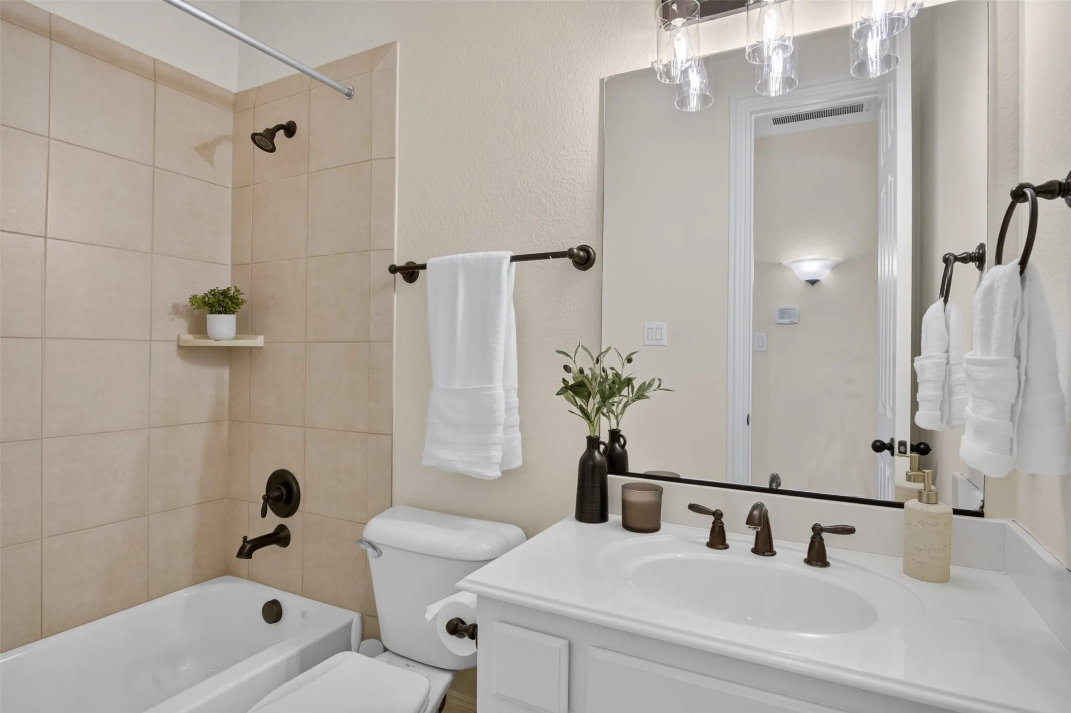 Bathroom featuring a tub/shower combination with tiled surround, a single vanity with an integrated sink, a large mirror, and bronze-finish fixtures