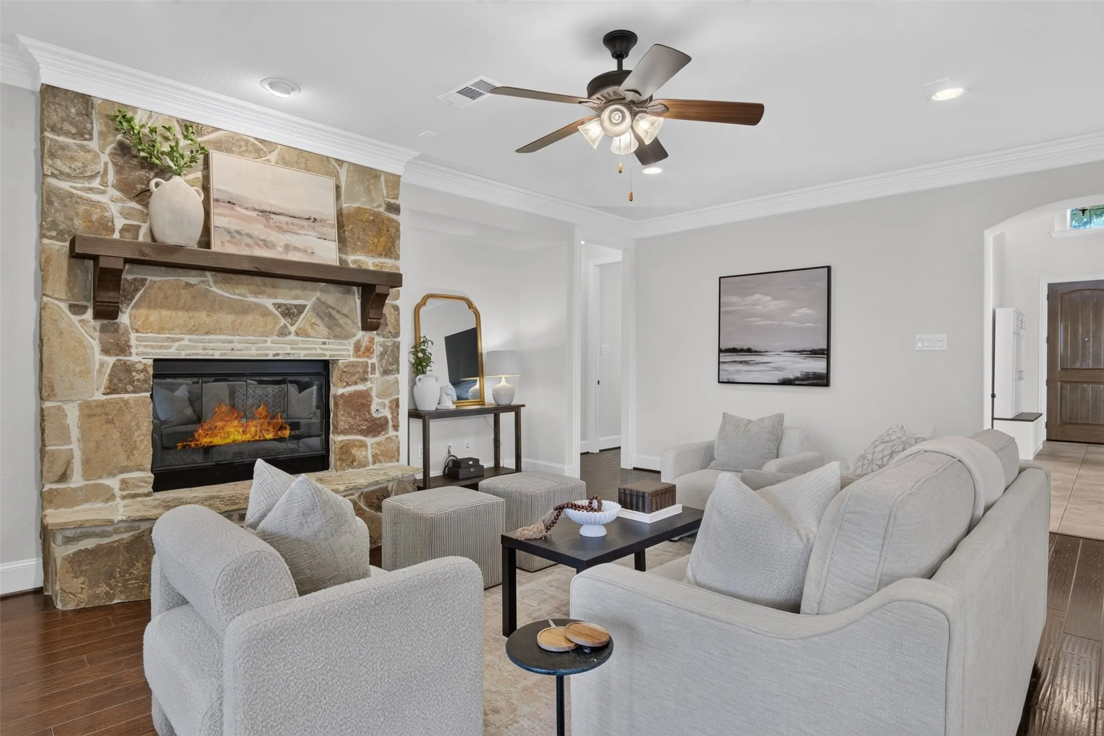 Stone-clad fireplace with wood mantel, crown molding, ceiling fan with light fixture, recessed lighting, and wood-finish flooring