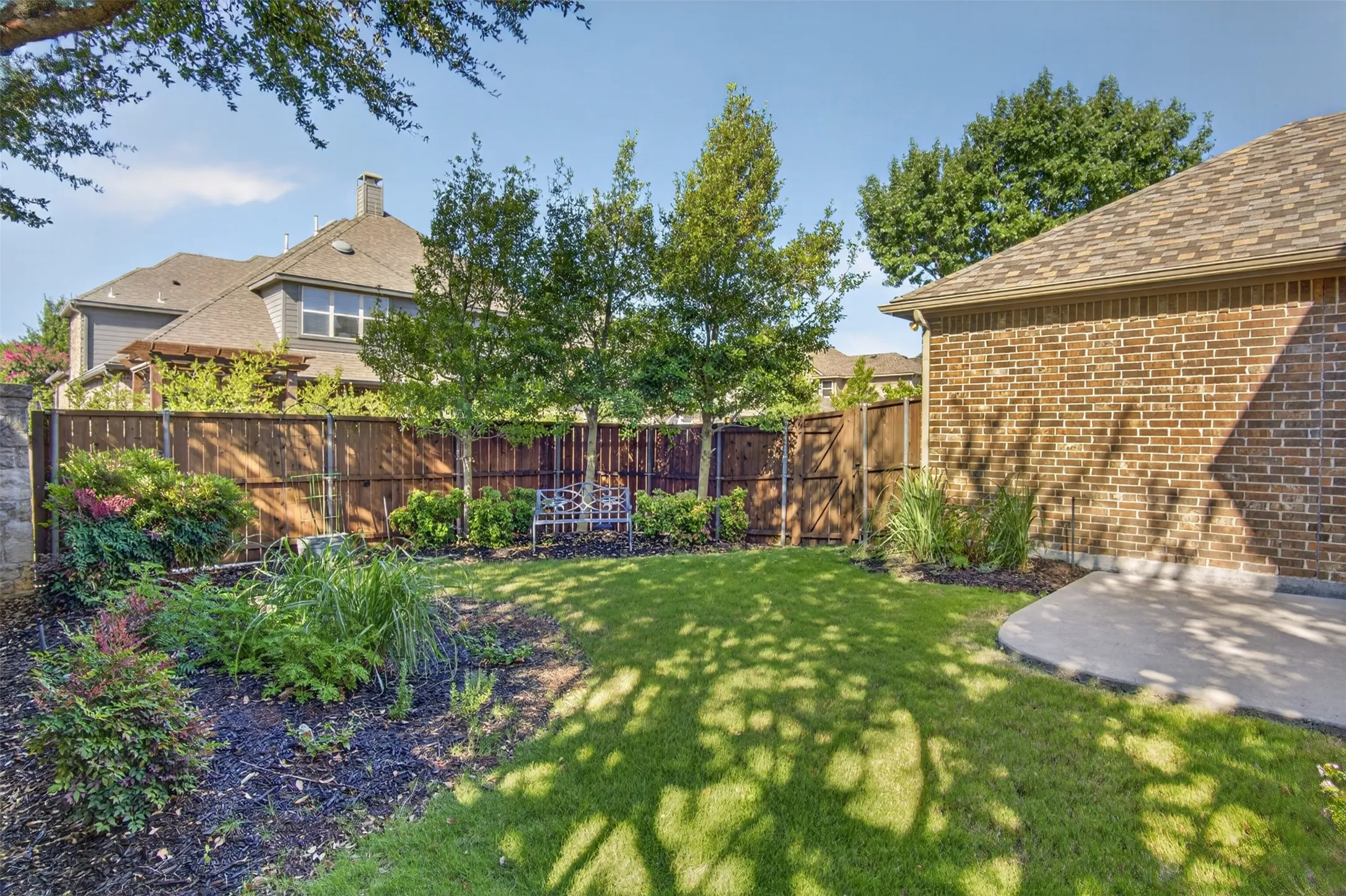 Expansive grassy yard with mature trees, established landscaping, privacy fencing, and a concrete patio