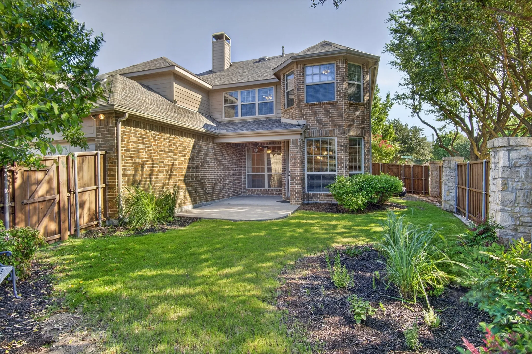 Brick exterior with multiple windows, a rear patio, and a fenced yard with mature landscaping
