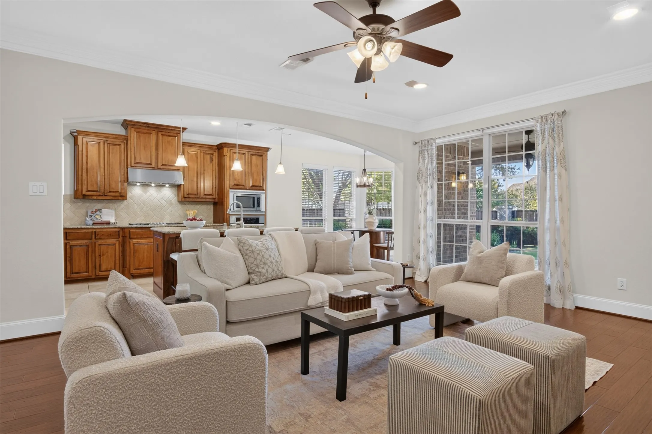 Hardwood flooring, crown molding, arched room entry, ceiling fan with integrated lighting, and a kitchen with wood cabinetry