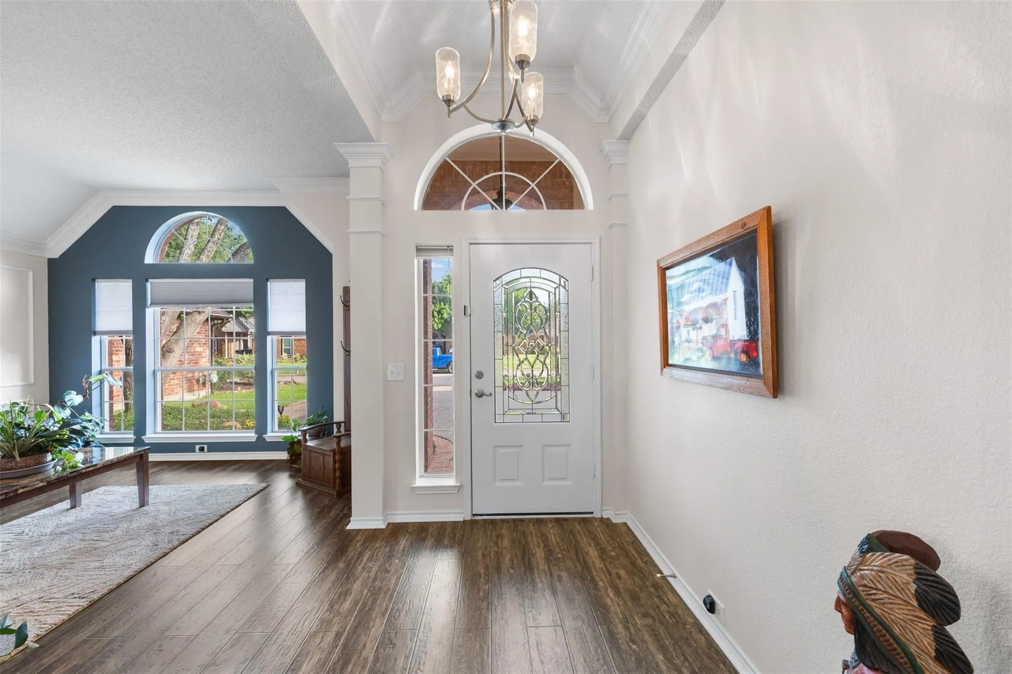 Wood-finish flooring, decorative front door with arched transom, chandelier lighting, and a large picture window with an arched transom