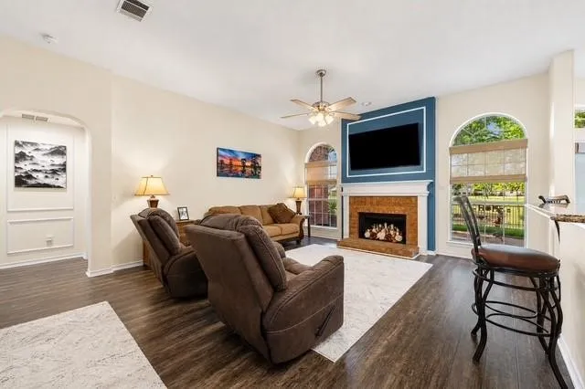 Living area featuring wood-finish flooring, an arched entryway, a ceiling fan with light fixture, and arched windows with blinds