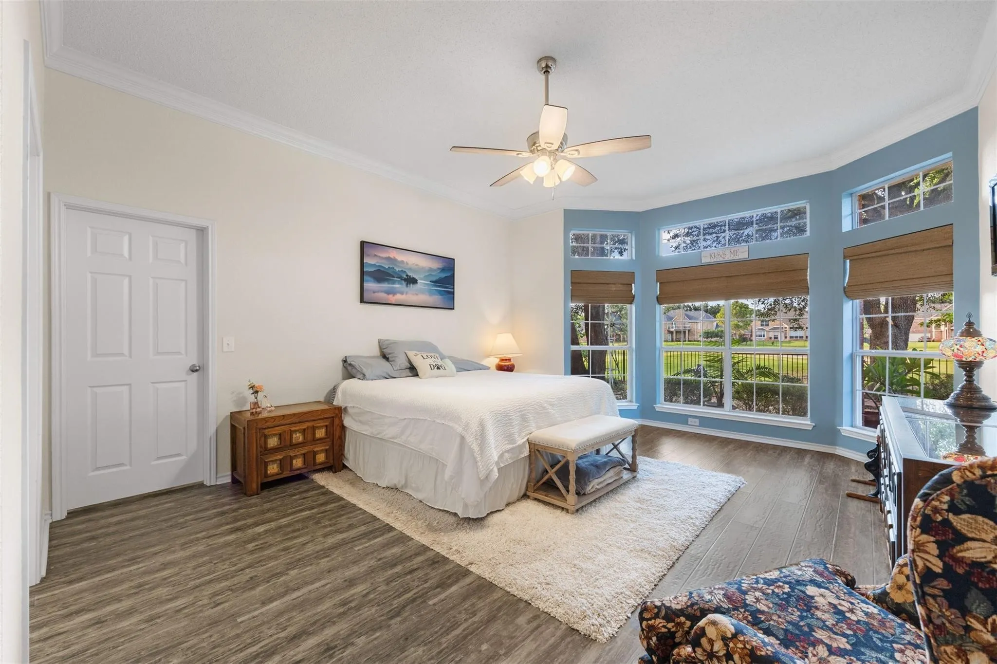 Bay window with multiple panes, wood-finish flooring, ceiling fan, and crown molding