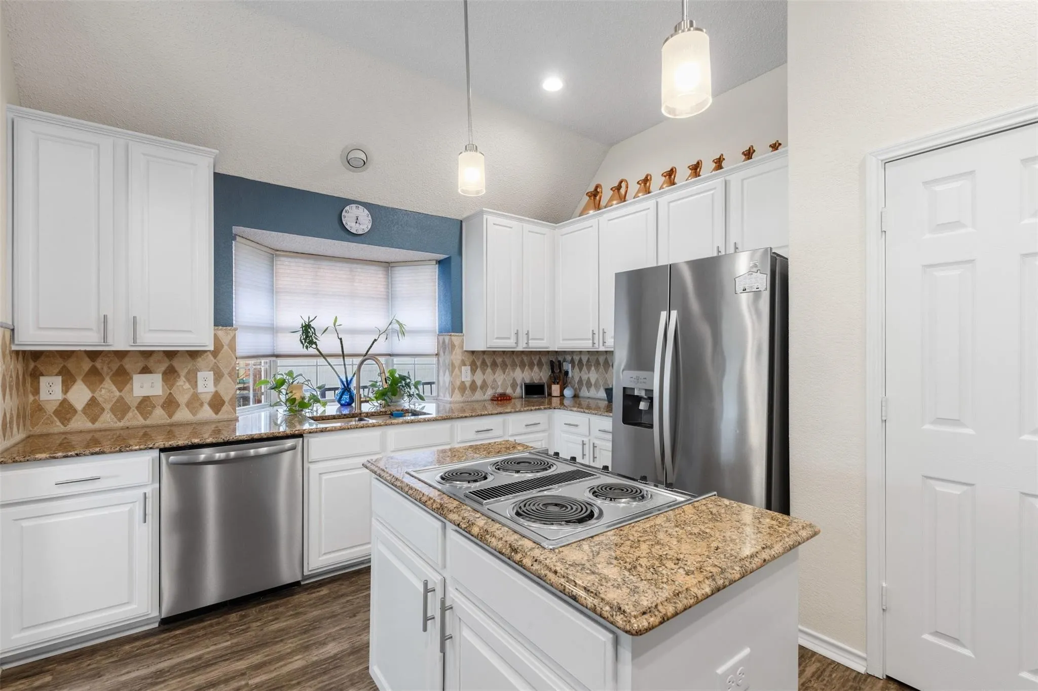 Kitchen with white shaker-style cabinetry, stainless steel appliances, granite countertops, patterned tile backsplash, and wood-finish flooring