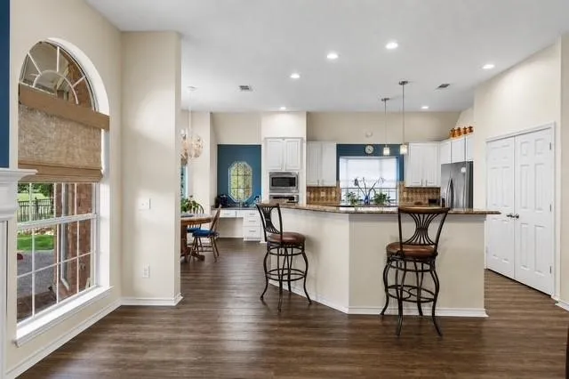 Spacious kitchen featuring an expansive counter-height island, wood-finish flooring, white cabinetry, and recessed lighting