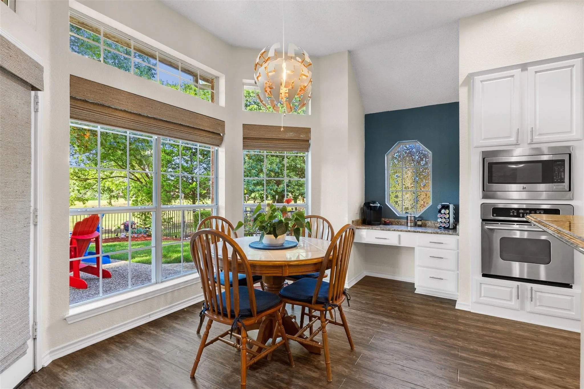 Wood-finish flooring, built-in stainless steel microwave and oven, white cabinetry, granite countertop, and large windows with transom architectural details