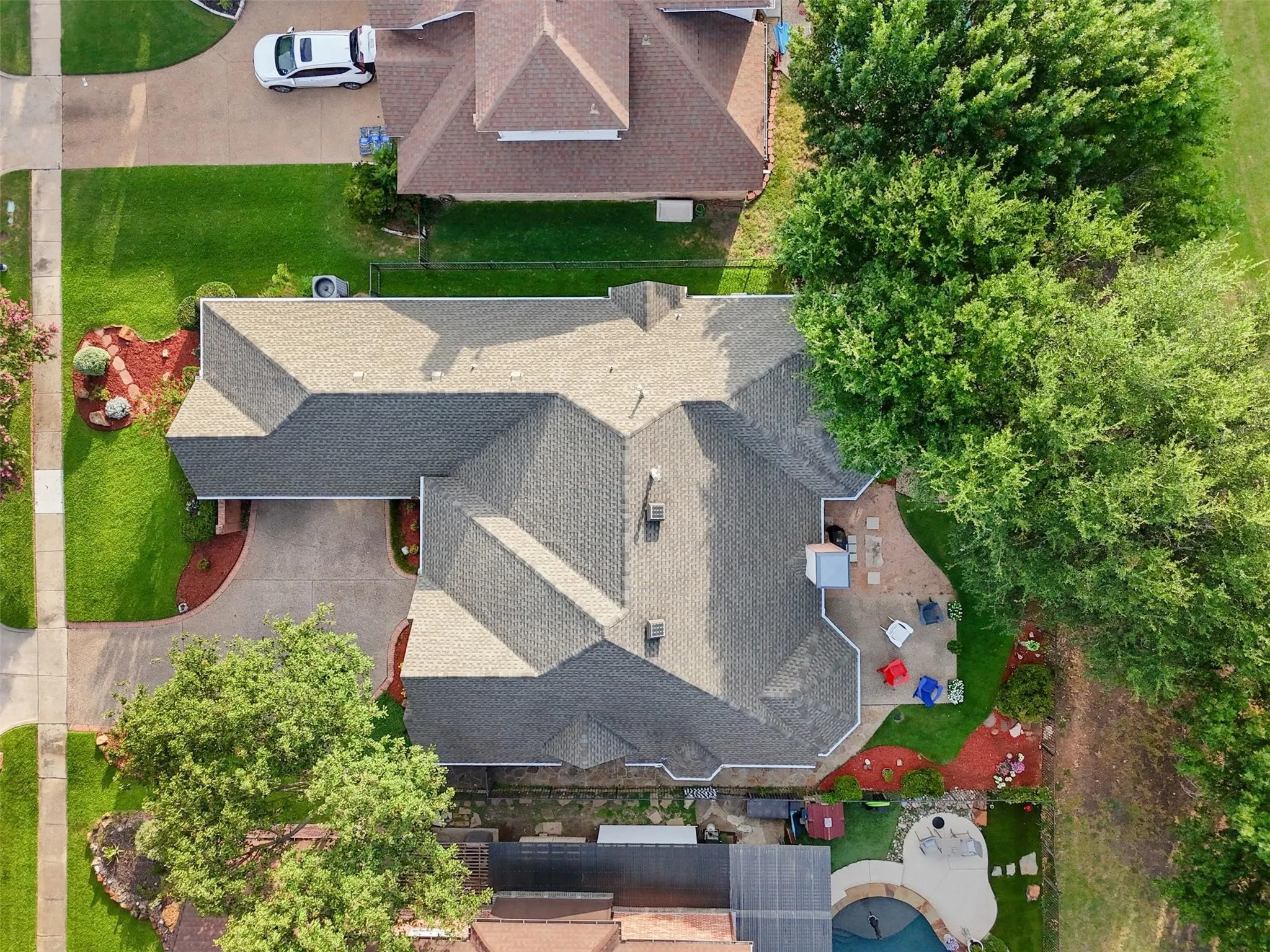 Gabled roofline, concrete driveway, front yard landscaping, rear patio with paved hardscaping, and a swimming pool