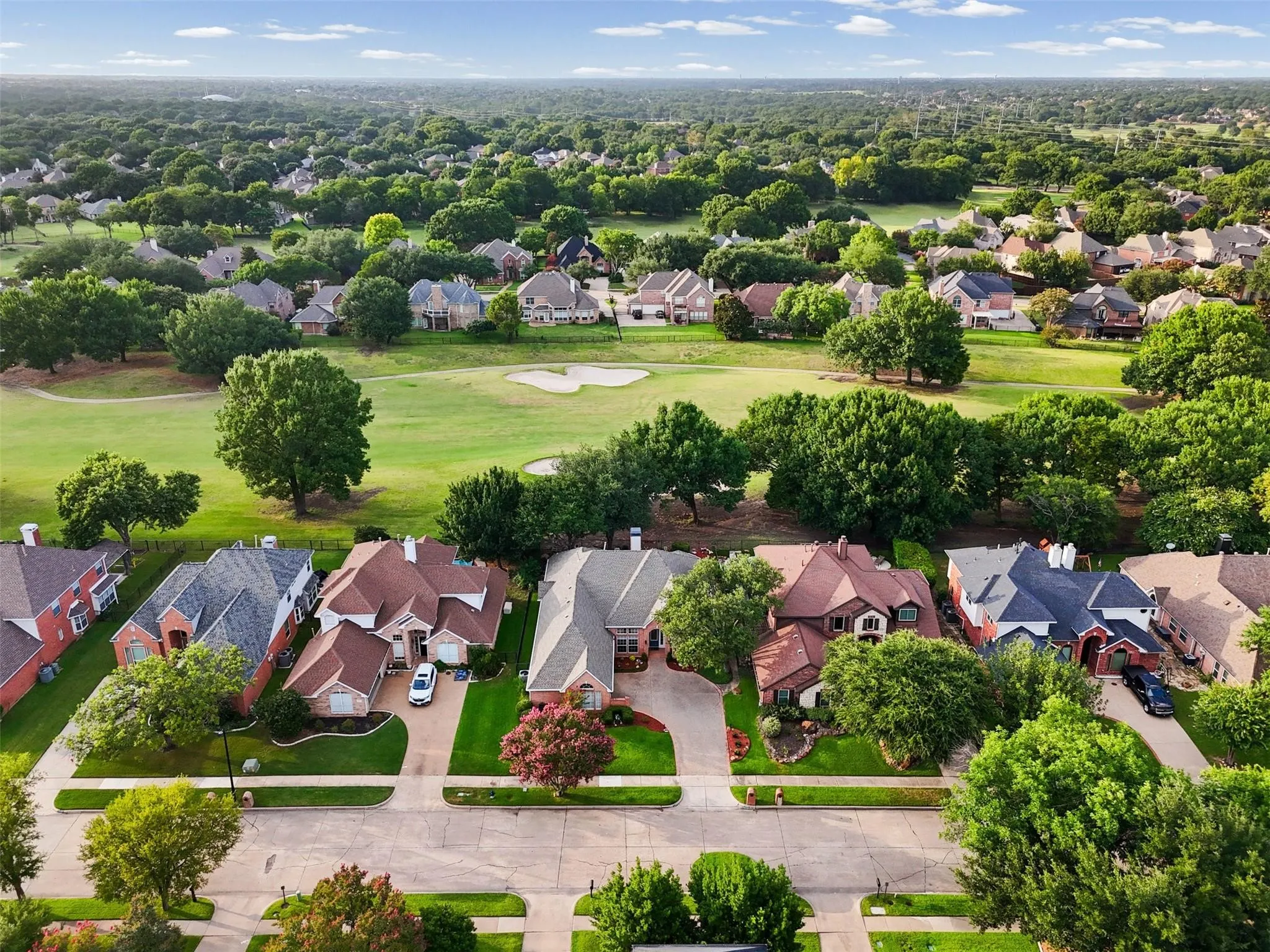 Residential street with manicured lawns, mature trees, and a golf course backing the properties