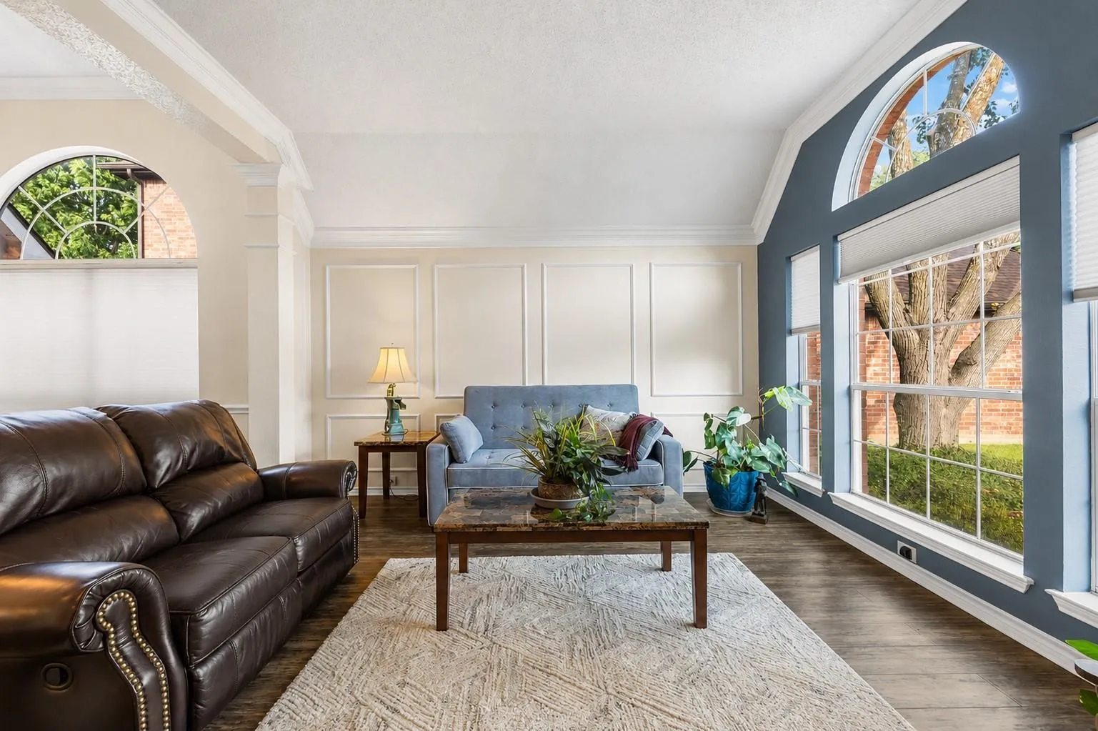 Vaulted ceiling, paneled accent wall, wood-finish flooring, arched window, and large bay windows