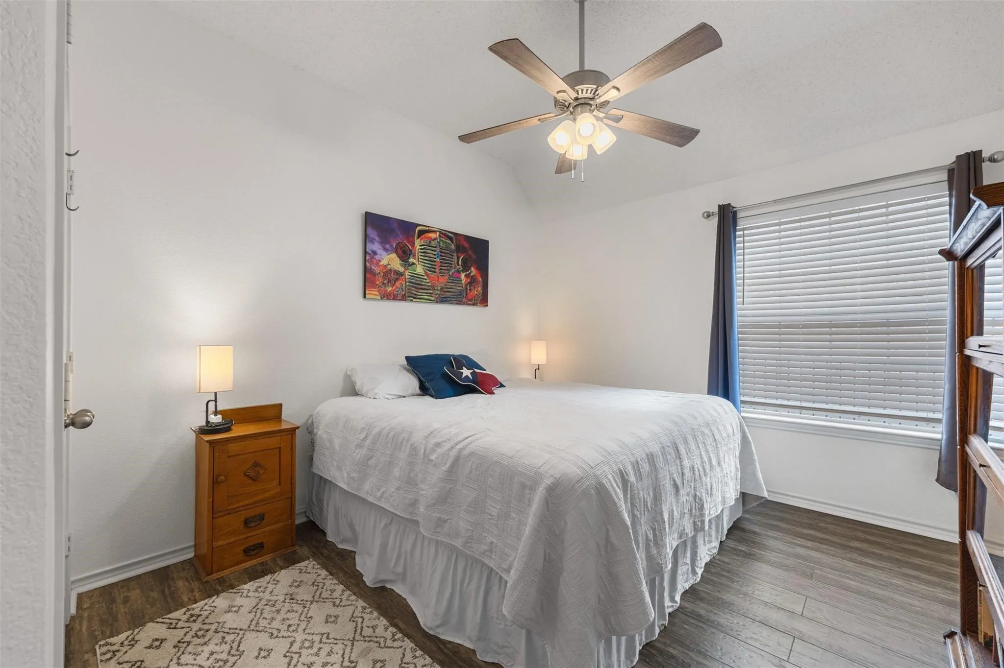 Vaulted ceiling, wood-finish flooring, ceiling fan with integrated lighting, window with blinds, and white walls