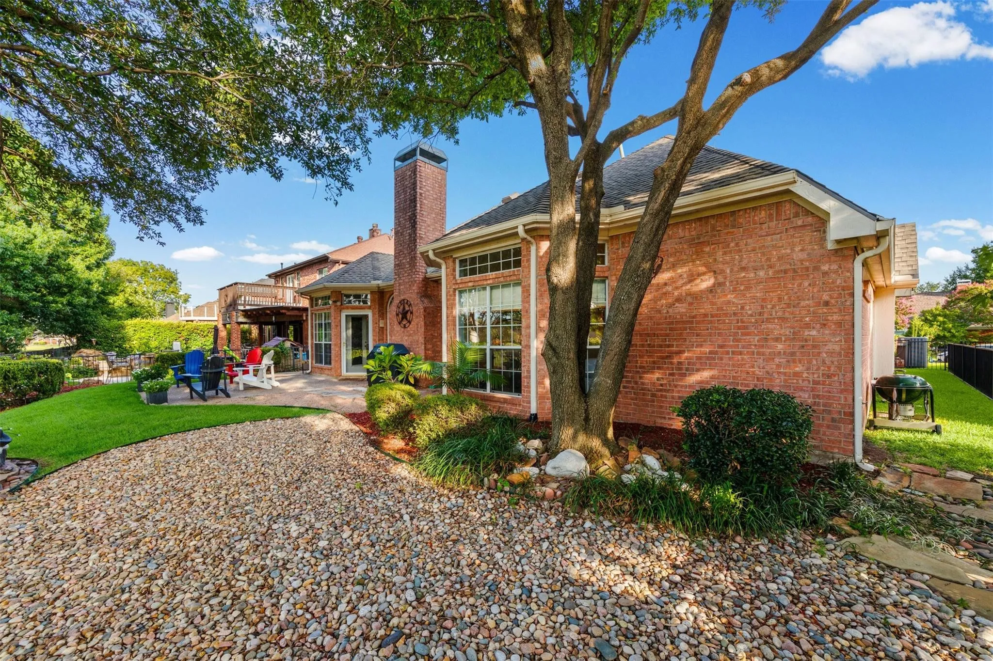 Brick exterior with a stone patio, mature landscaping, and a gravel pathway