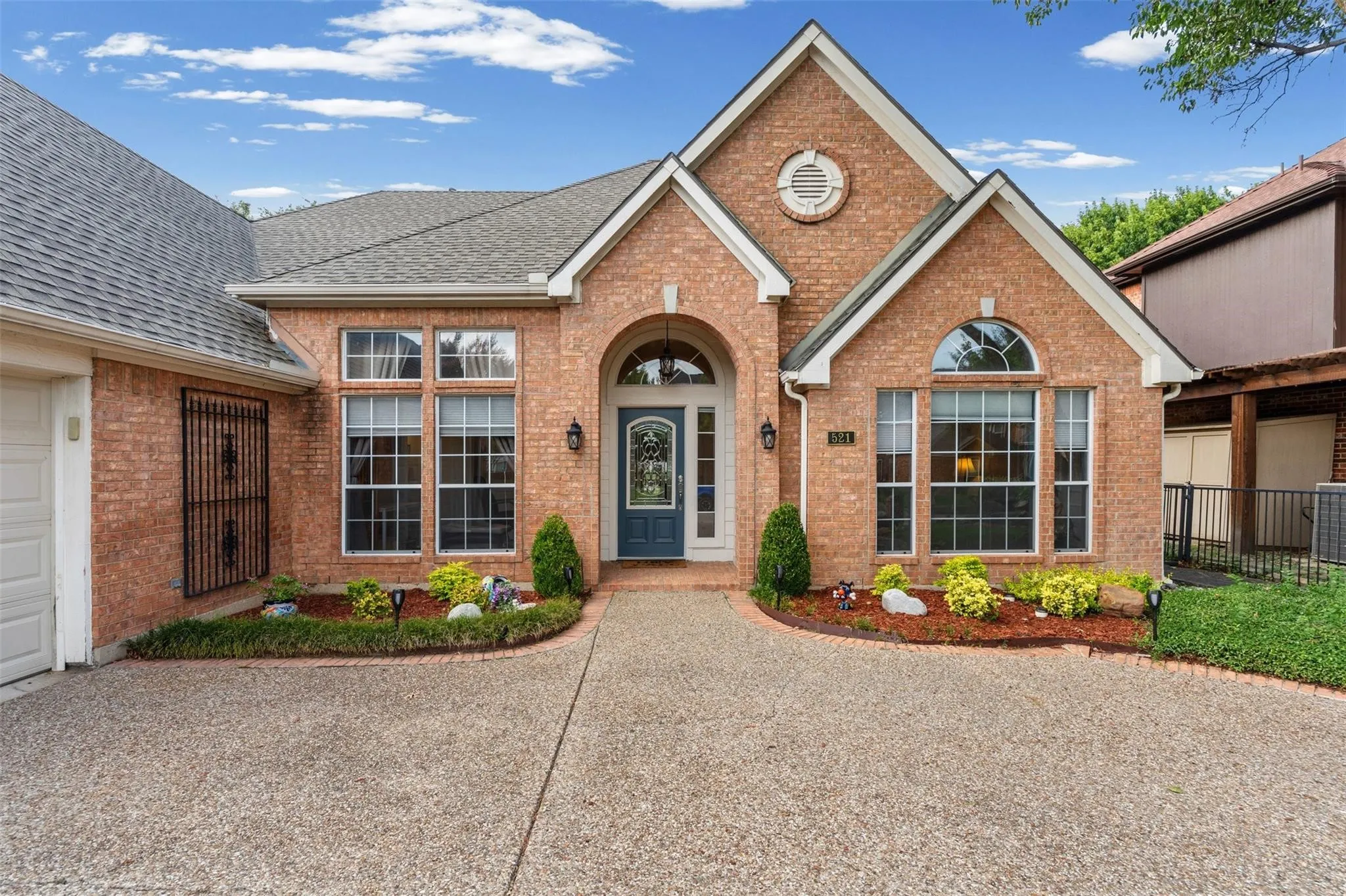 Brick exterior with a gabled roofline, arched entry, decorative front door, and mature landscaping