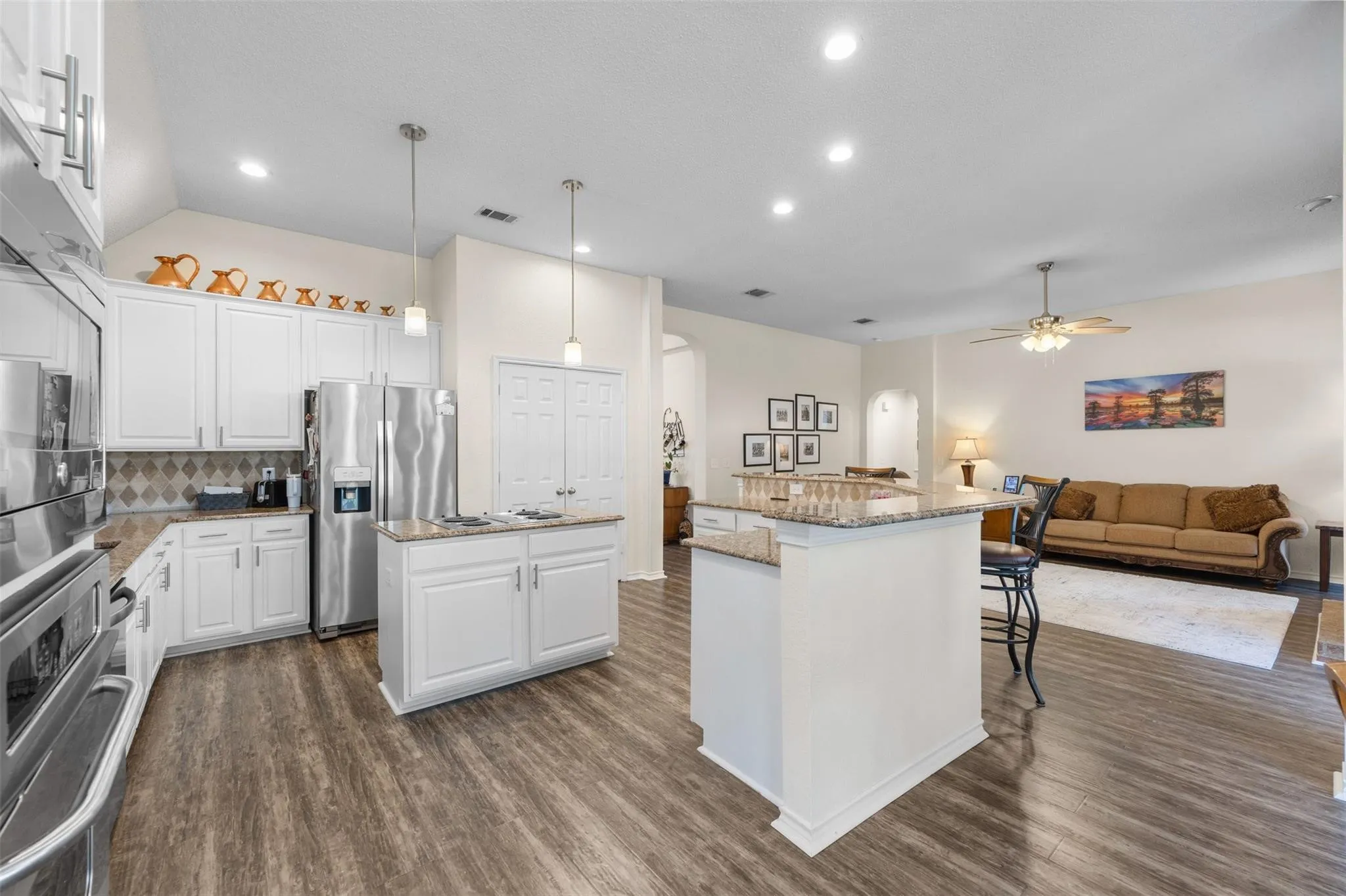 Kitchen with wood-finish flooring, white cabinetry, stainless steel appliances, and a central island with a granite countertop