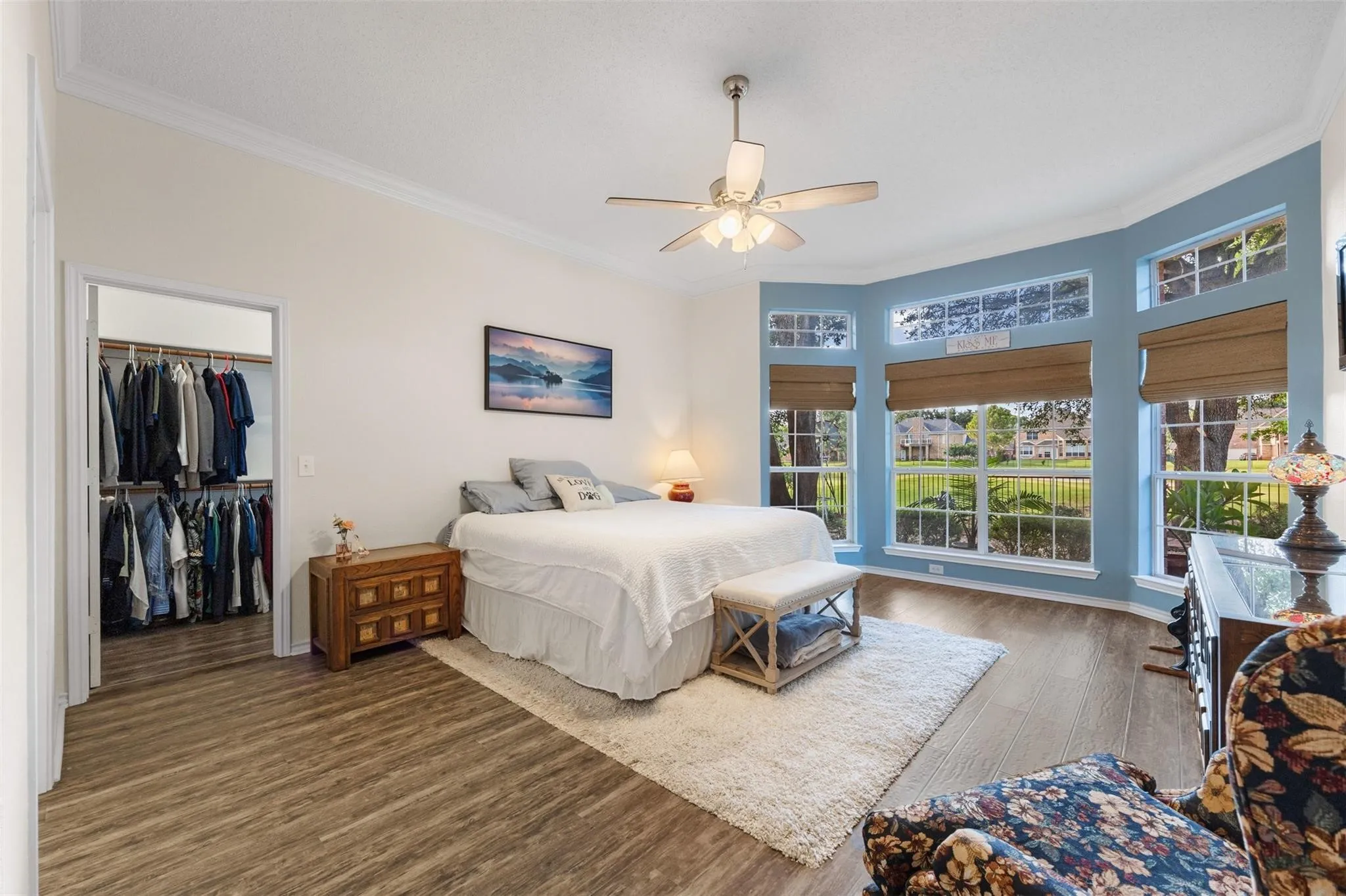Bay window with multiple windows, crown molding, wood-finish flooring, ceiling fan, and walk-in closet