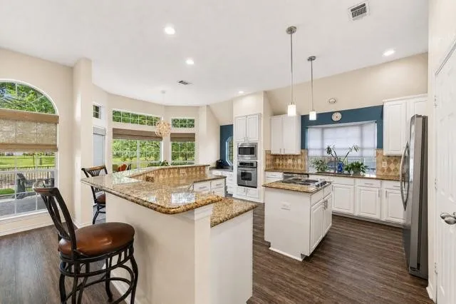 Kitchen featuring wood-finish flooring, white cabinetry, a central island with cooktop, and built-in stainless steel appliances