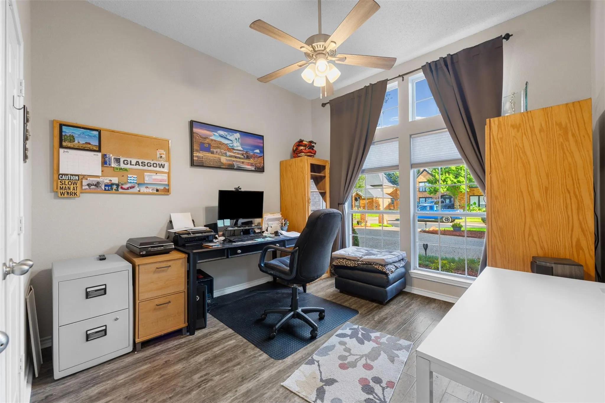 Wood-finish flooring, ceiling fan with integrated lighting, and multiple windows providing ample natural illumination