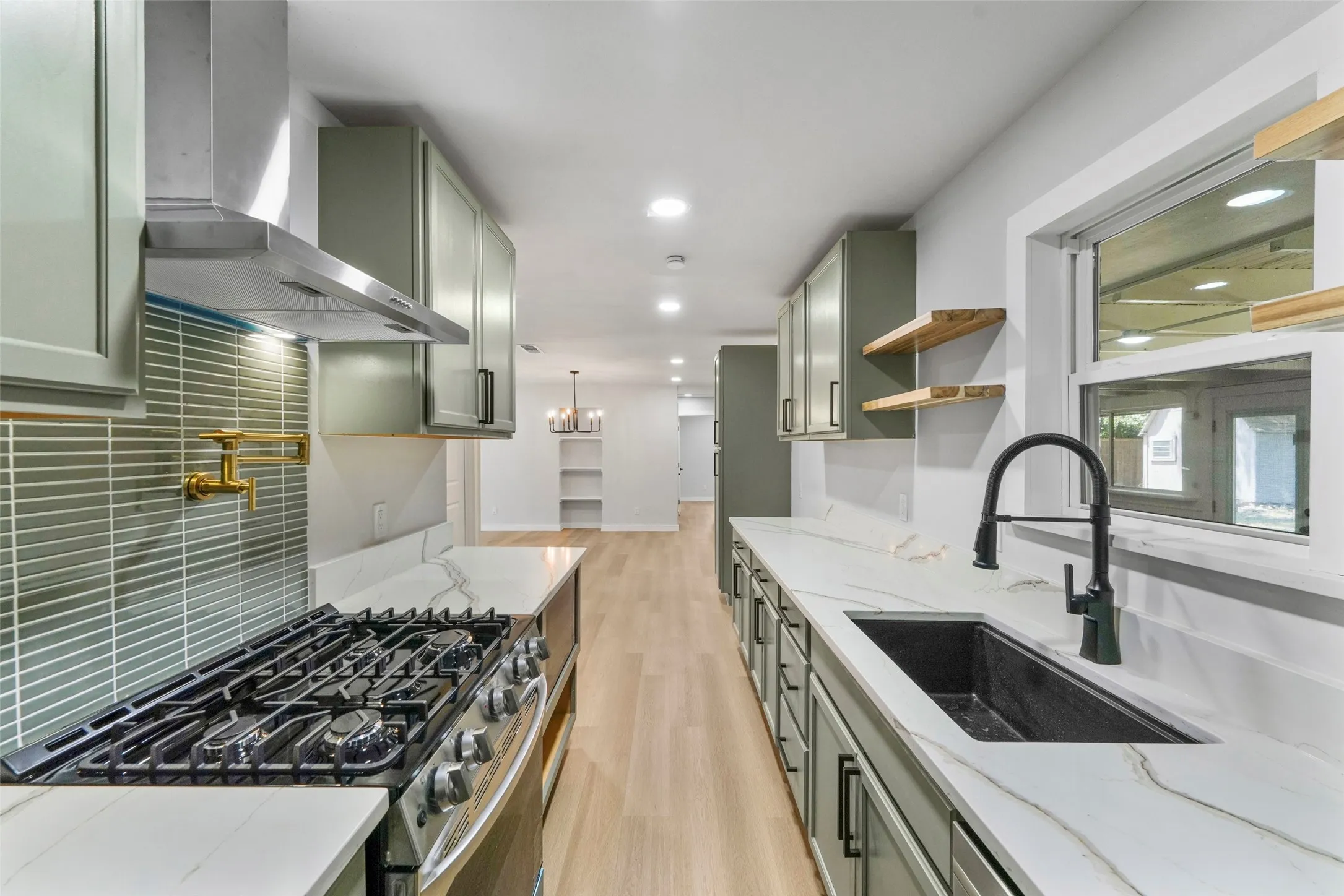 Modern kitchen featuring light green cabinetry, white countertops with veining, an undermount sink with a matte black faucet, wood-finish flooring, and a gas range with a stainless steel hood