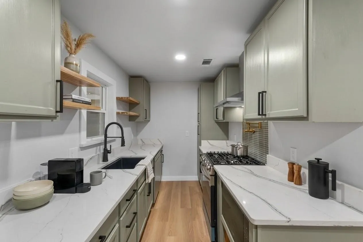 Galley kitchen featuring sage cabinetry, light-toned wood-finish flooring, white countertops with veining, and a stainless steel gas range with a tile backsplash