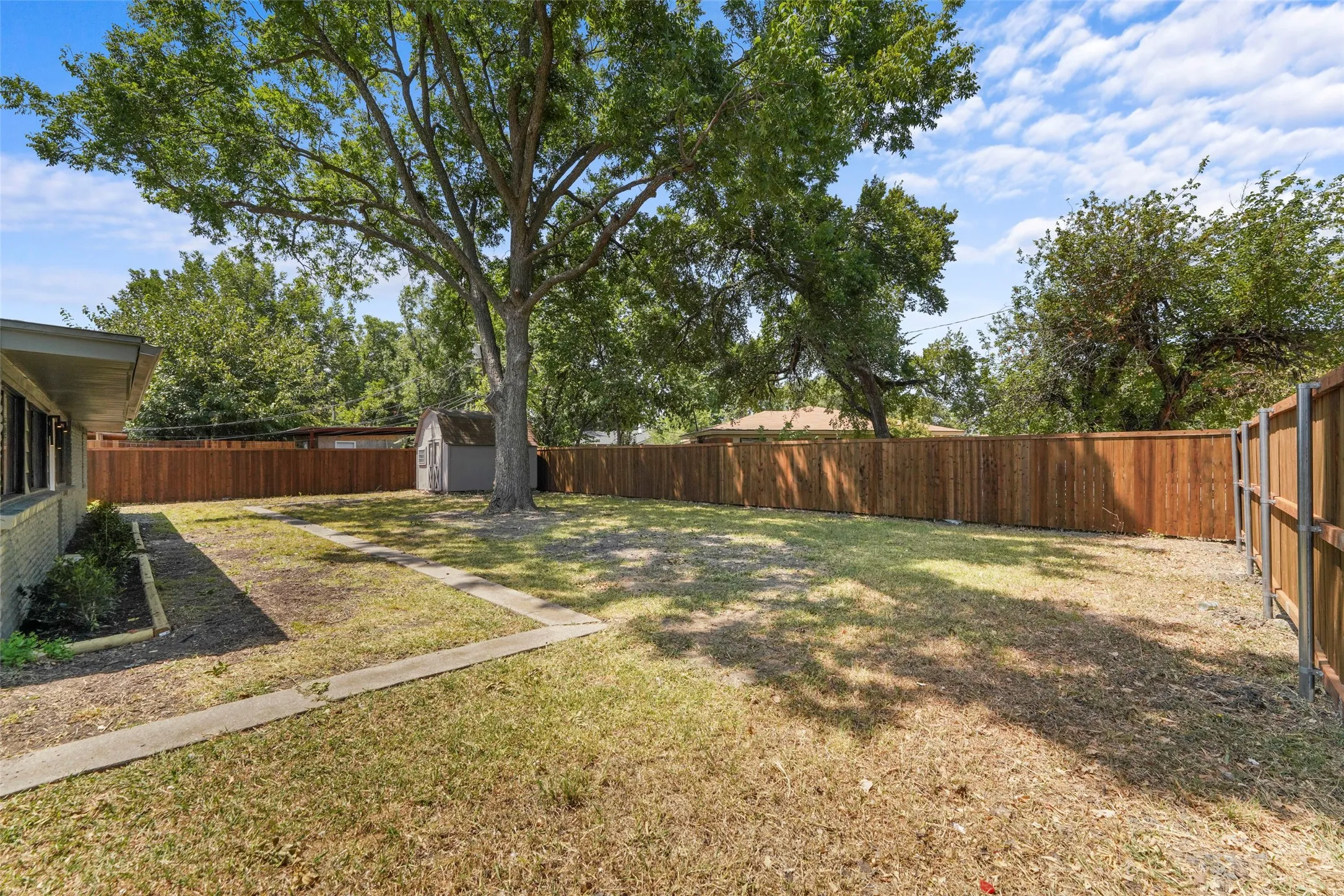 Expansive backyard with a manicured lawn, established shade tree, and wood privacy fencing