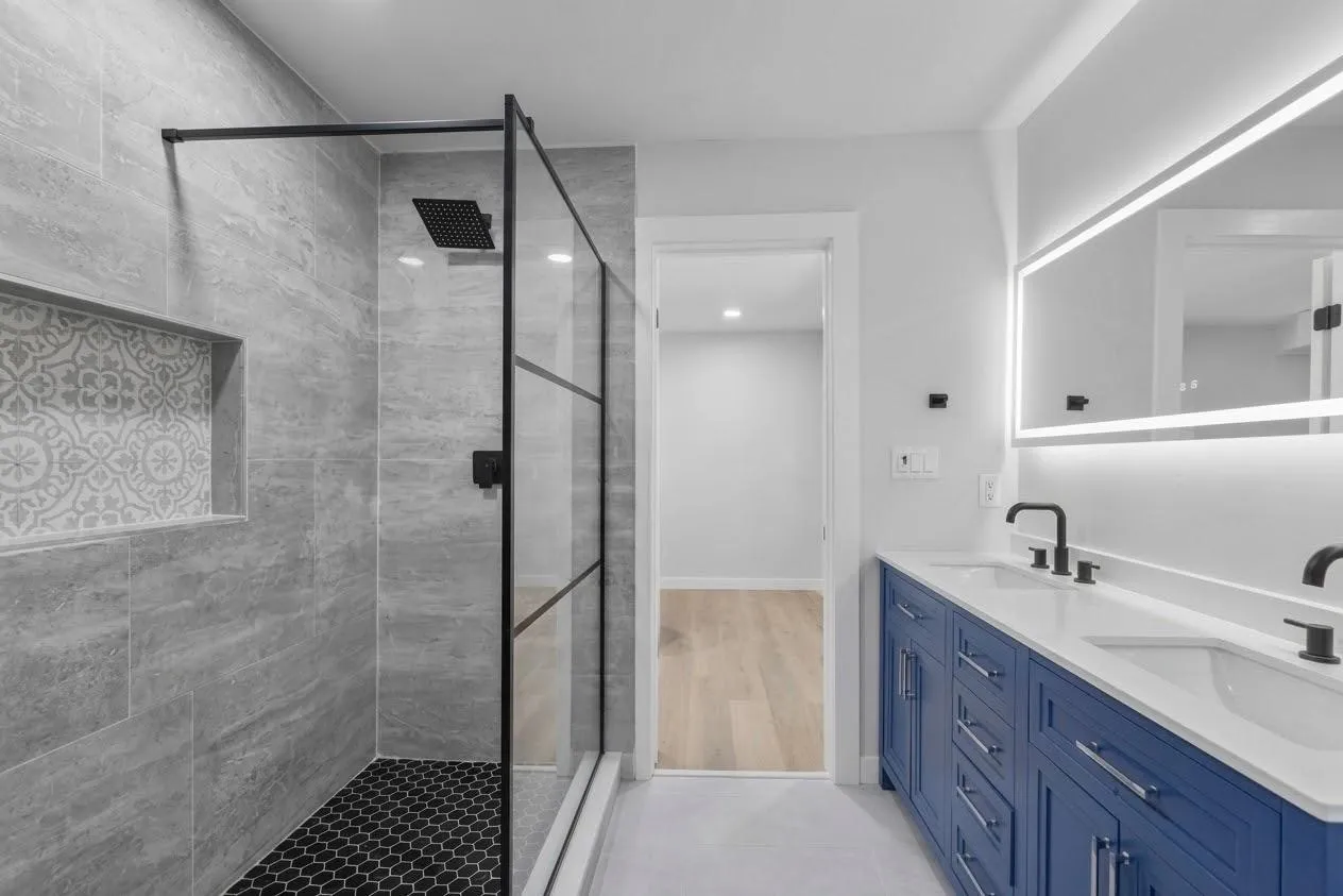 Shower with gray tile surround, patterned accent niche, and black hexagonal floor tiling