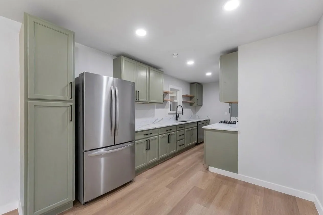 Modern kitchen featuring wood-finish flooring, recessed lighting, green cabinetry, stainless steel appliances, and white countertops