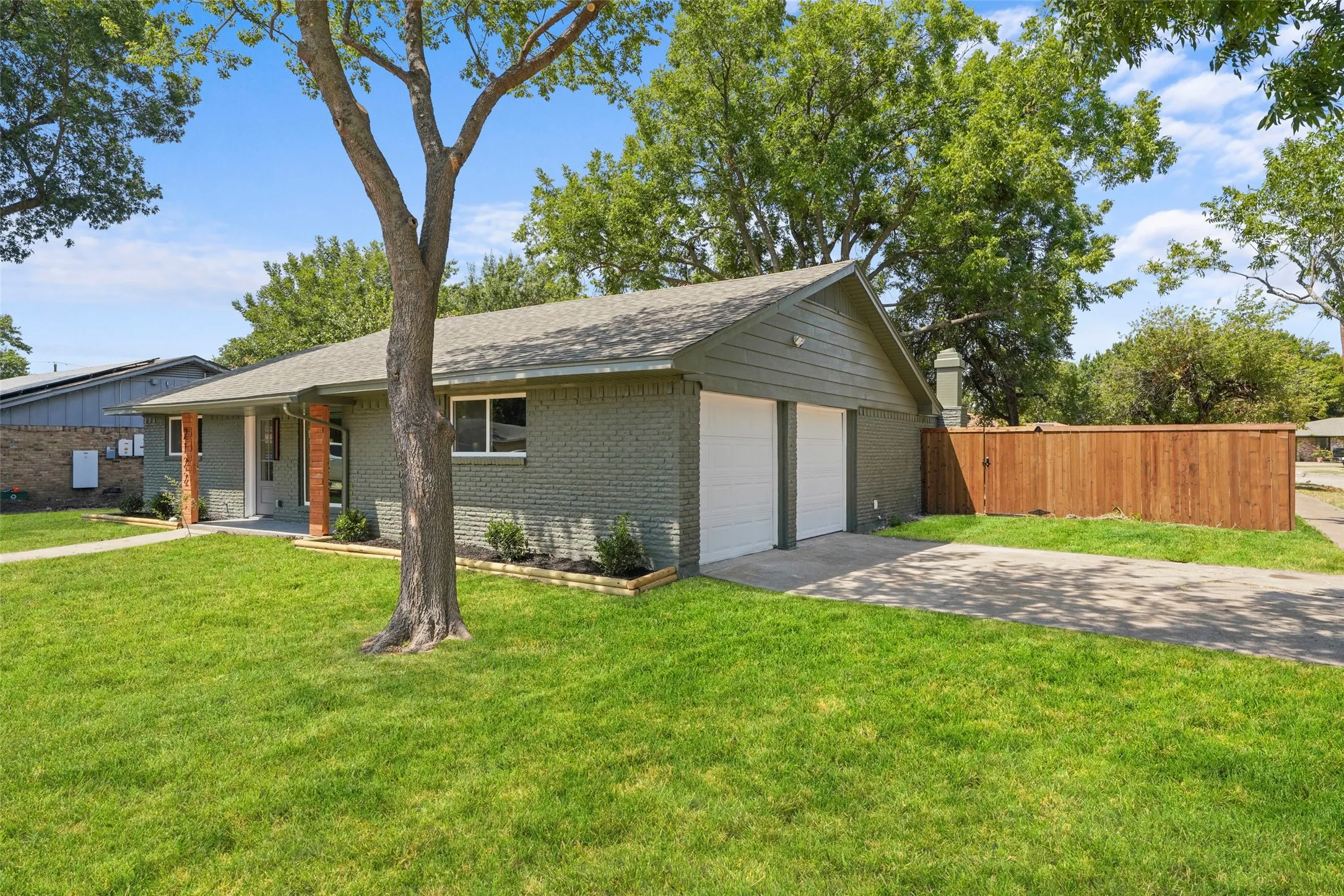 Brick exterior with a gabled roofline, two-car garage, concrete driveway, and a wood privacy fence
