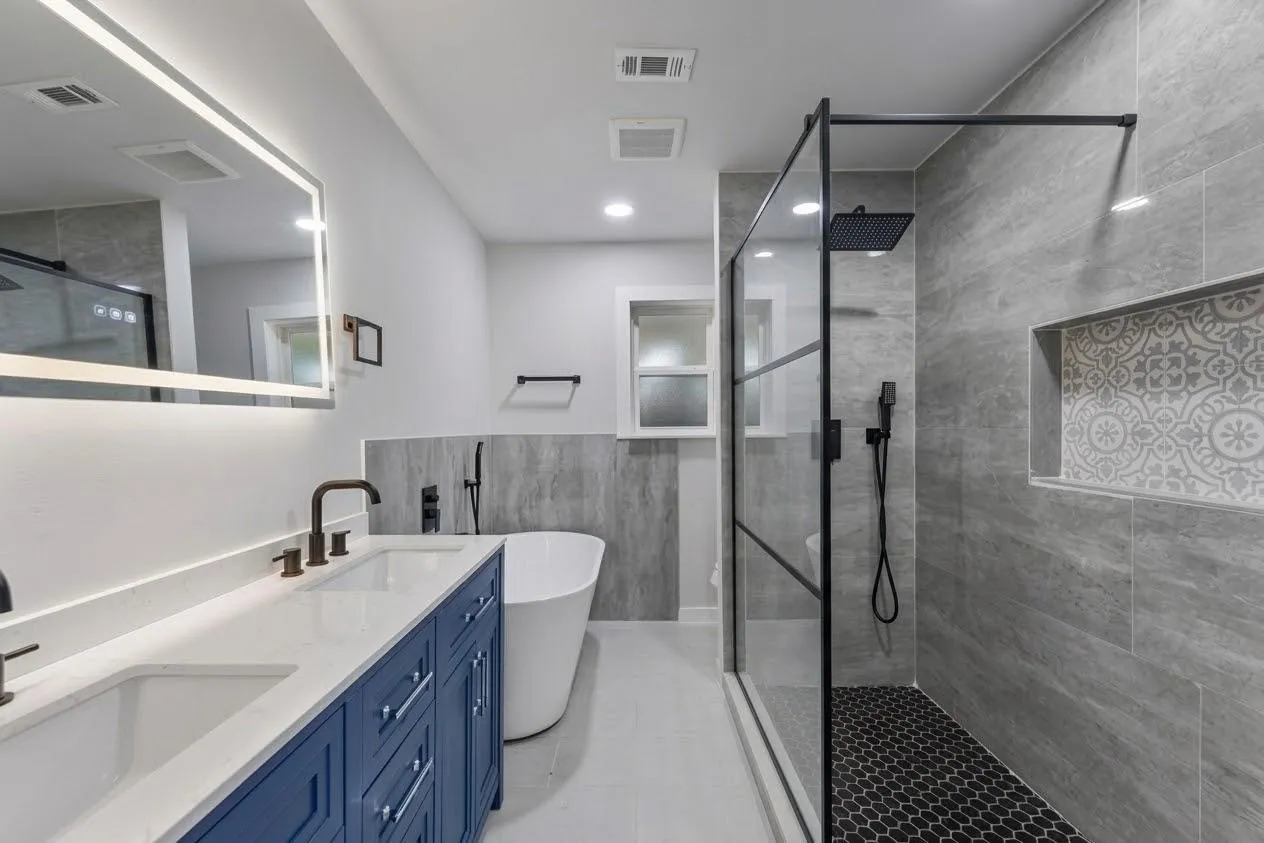 Dual vanity with white countertops and blue cabinetry, freestanding soaking tub, frameless glass shower with black fixtures, custom tiled shower niche, and recessed lighting