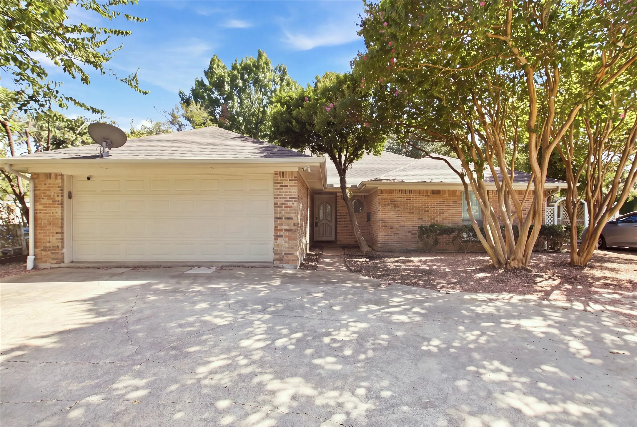 Brick exterior, attached two-car garage, mature trees, concrete driveway, and a gabled roof