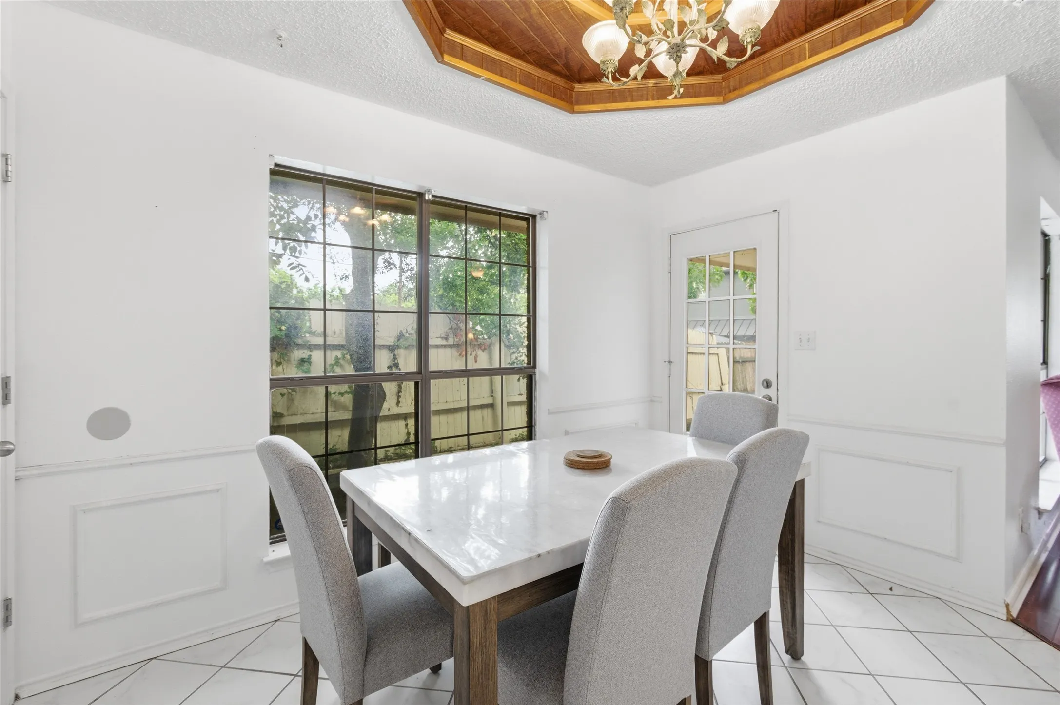 Wood-panel ceiling accent with a chandelier, large paneled window, white tile flooring, and wainscoting
