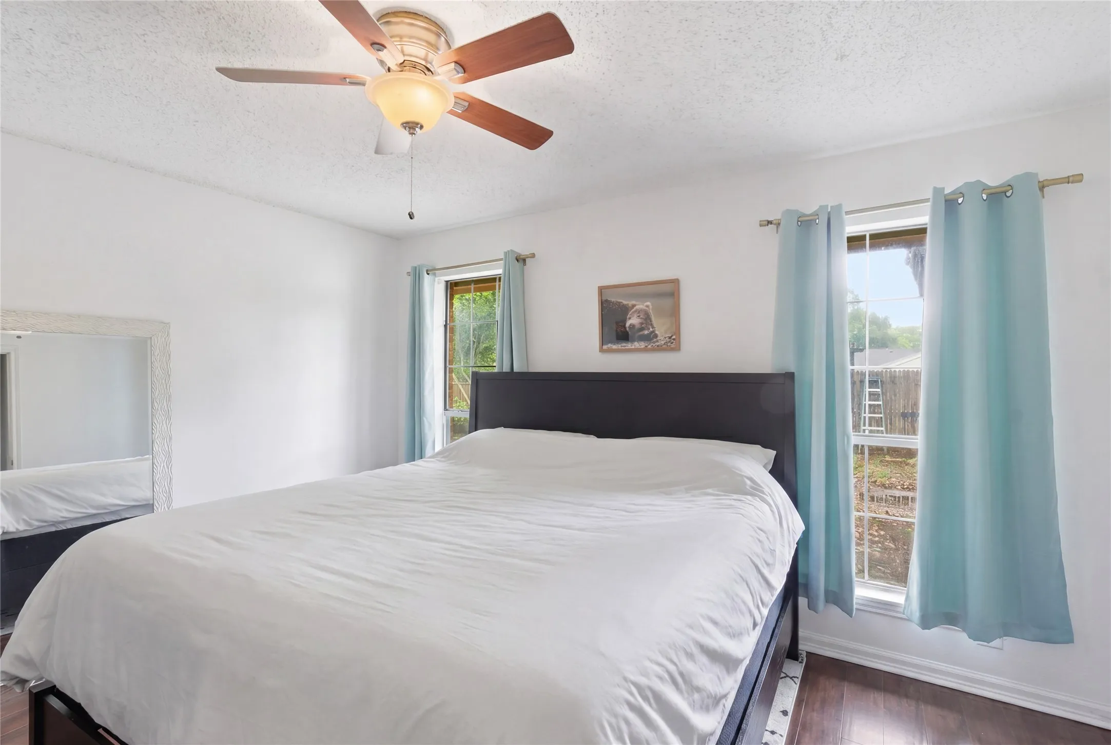 White walls, wood-finish flooring, two large windows, and a ceiling fan with integrated lighting