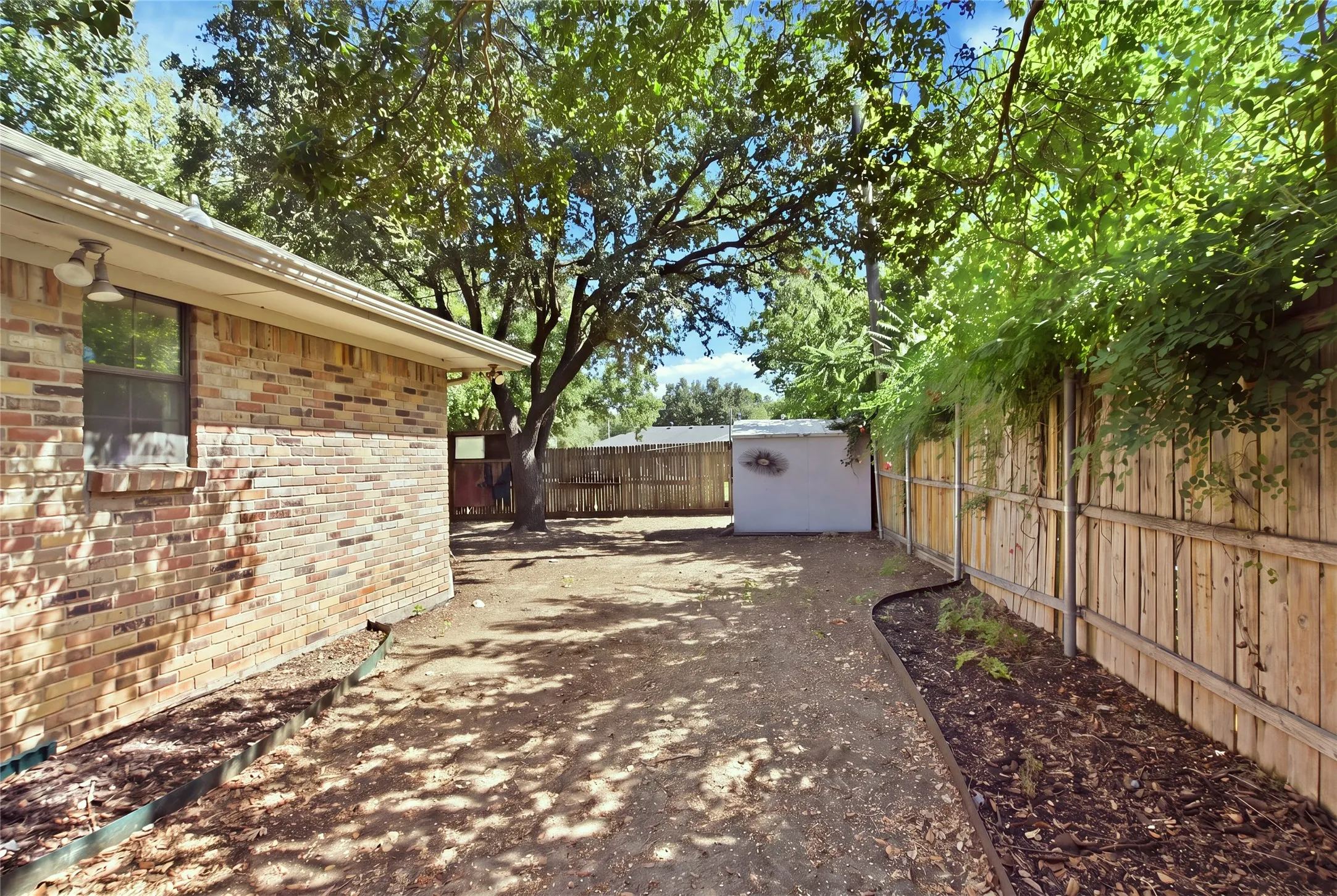 Spacious backyard with mature trees, a privacy fence, and a storage shed