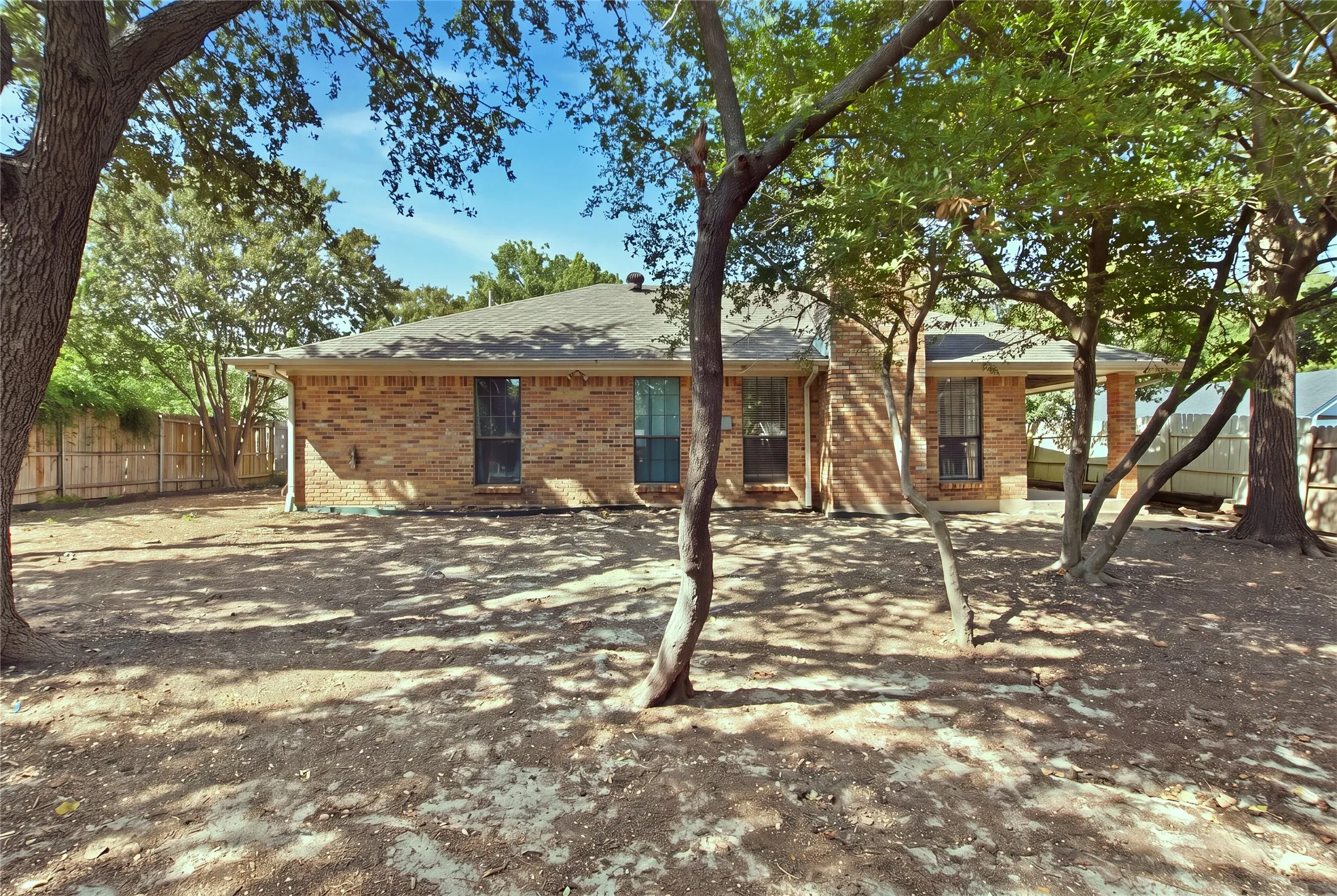 Brick exterior with a covered patio, multiple windows, and a shingled roof